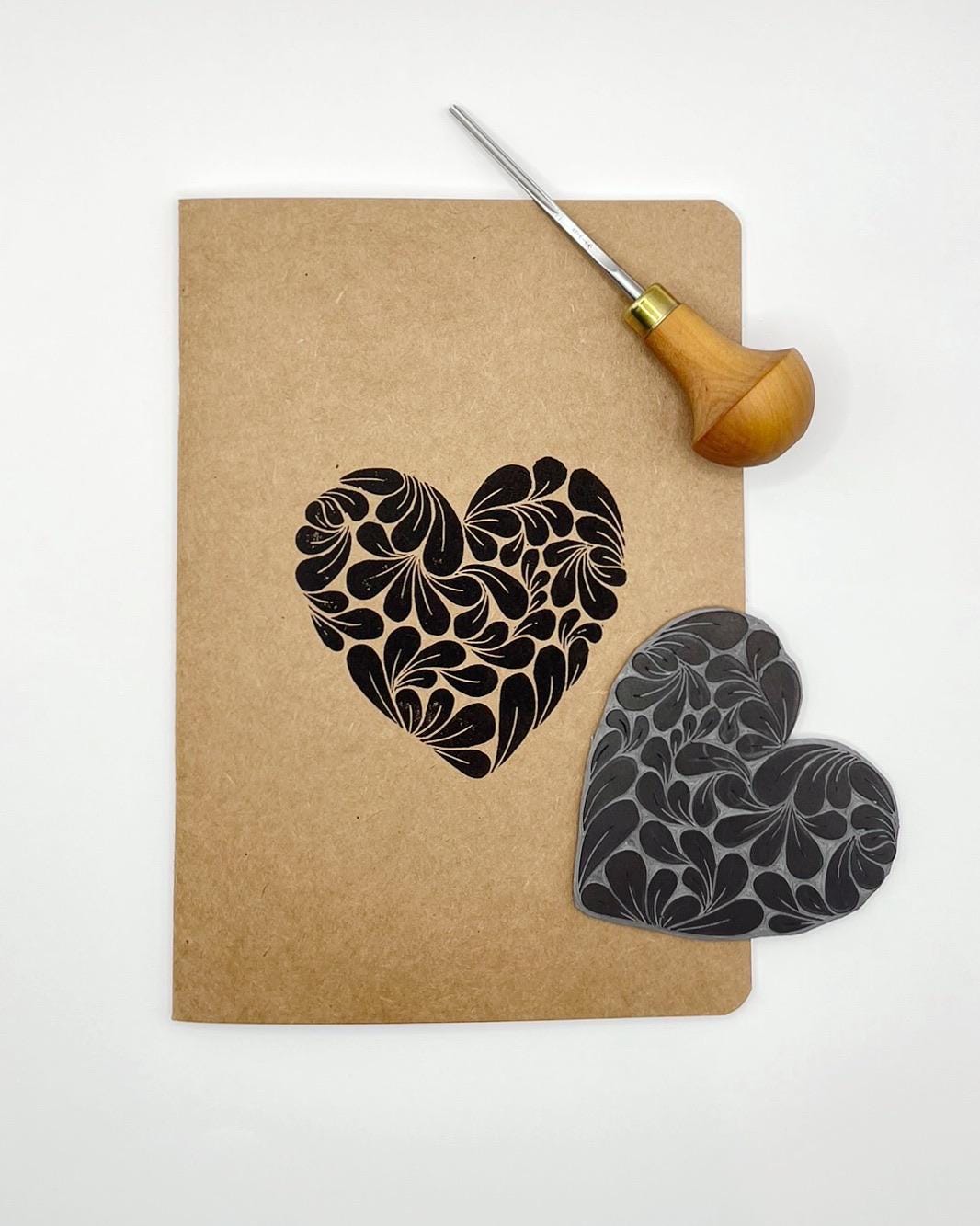 Floral heart design on a brown notebook with the lino and cutting tool included in the photo.