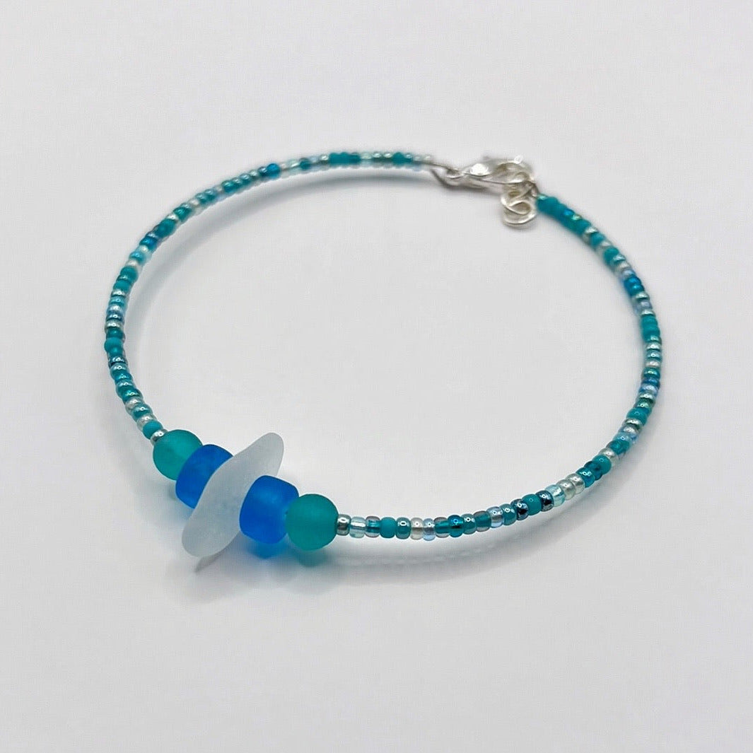 Bracelet with white sea glass and blue and turquoise beads laid on a white background