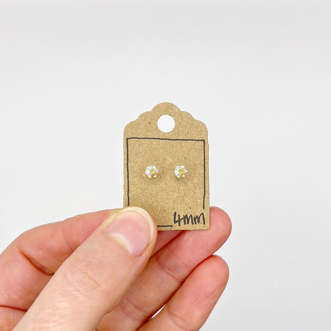 Small stud earrings on a cardboard backing held by a hand against a white background