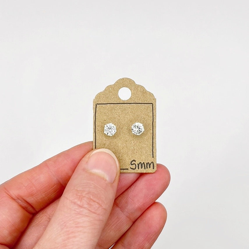 Clear cut glass stud earrings on a cardboard display card held by a hand against a white background