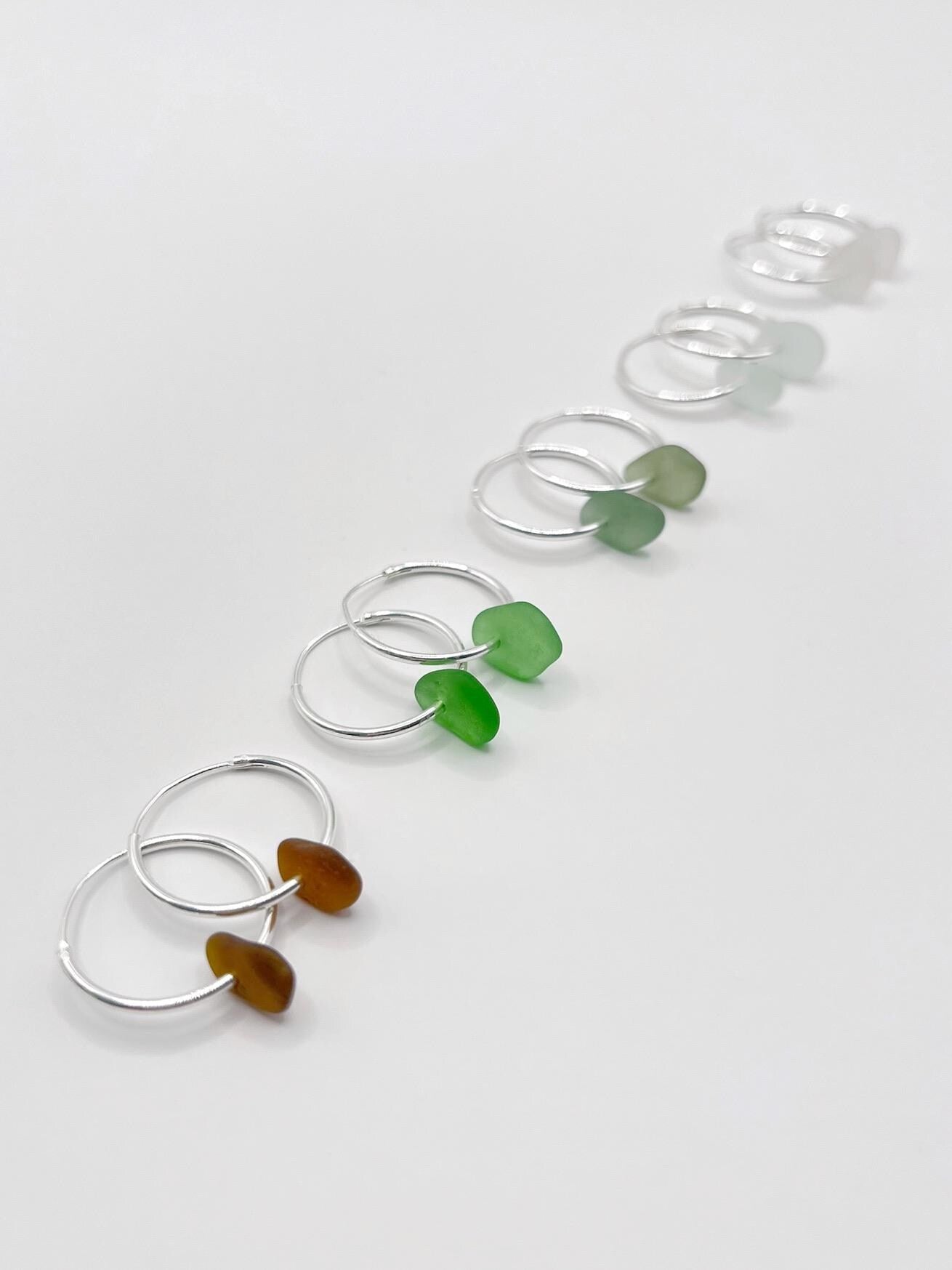Set of silver hoop earrings with coloured sea glass against a white background