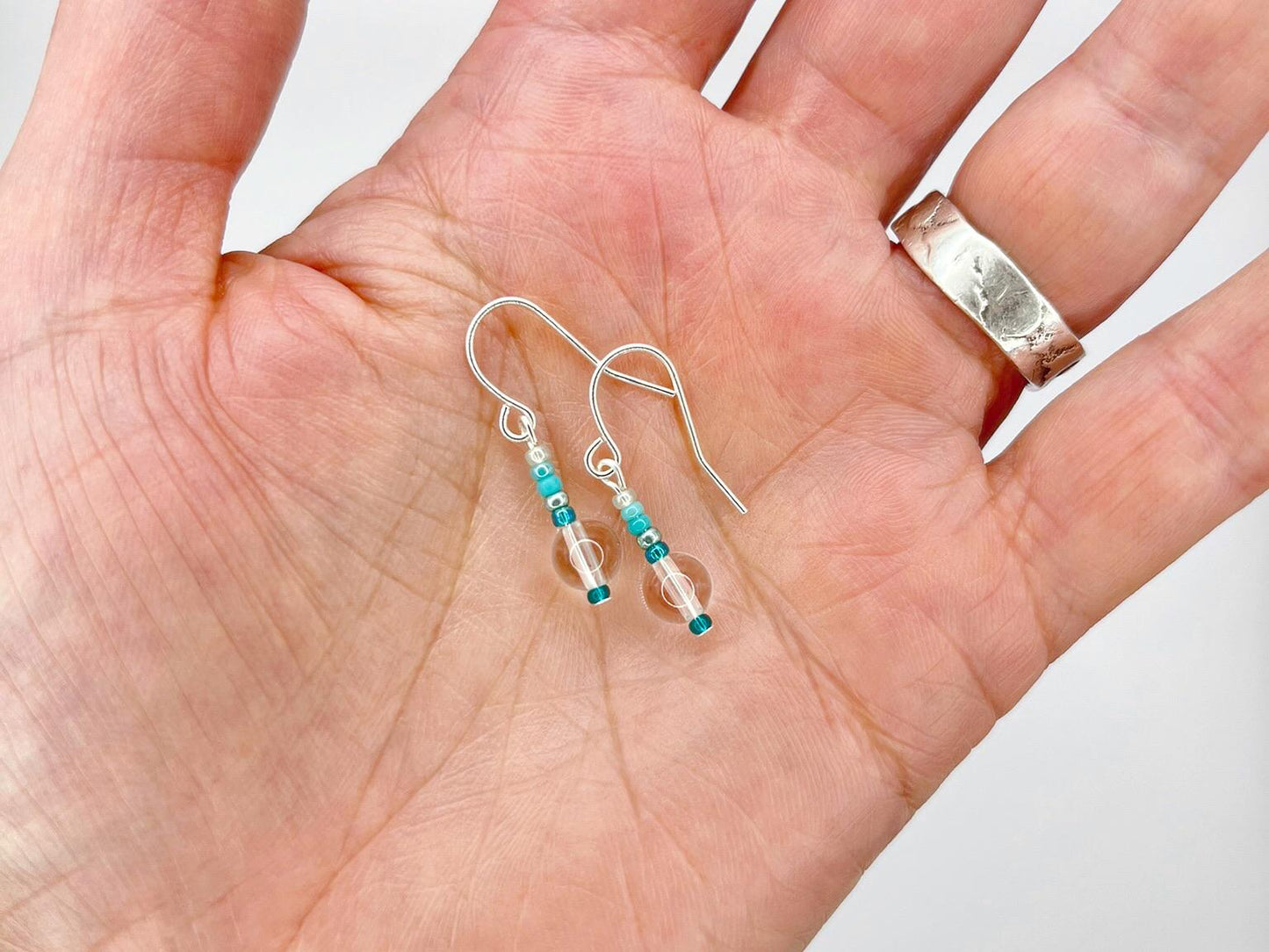 Silver earrings with clear crystal and turquoise seed beads held in a hand against a white background