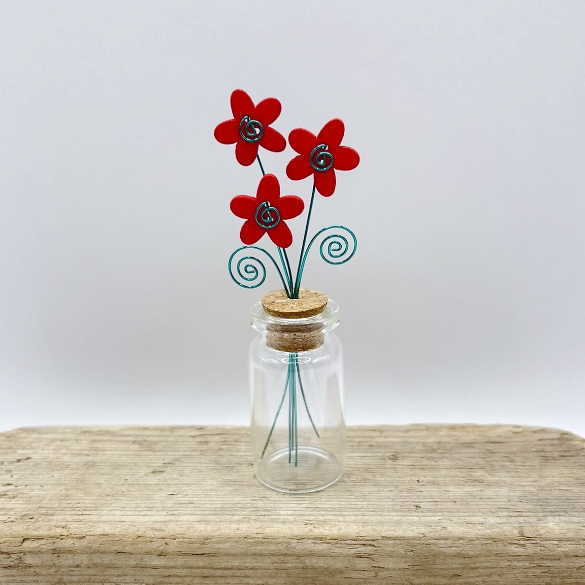 Little glass bottle with three red wooden flowers sat on driftwood