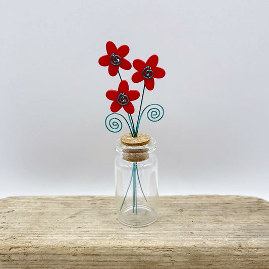 Little glass bottle with three red wooden flowers sat on driftwood