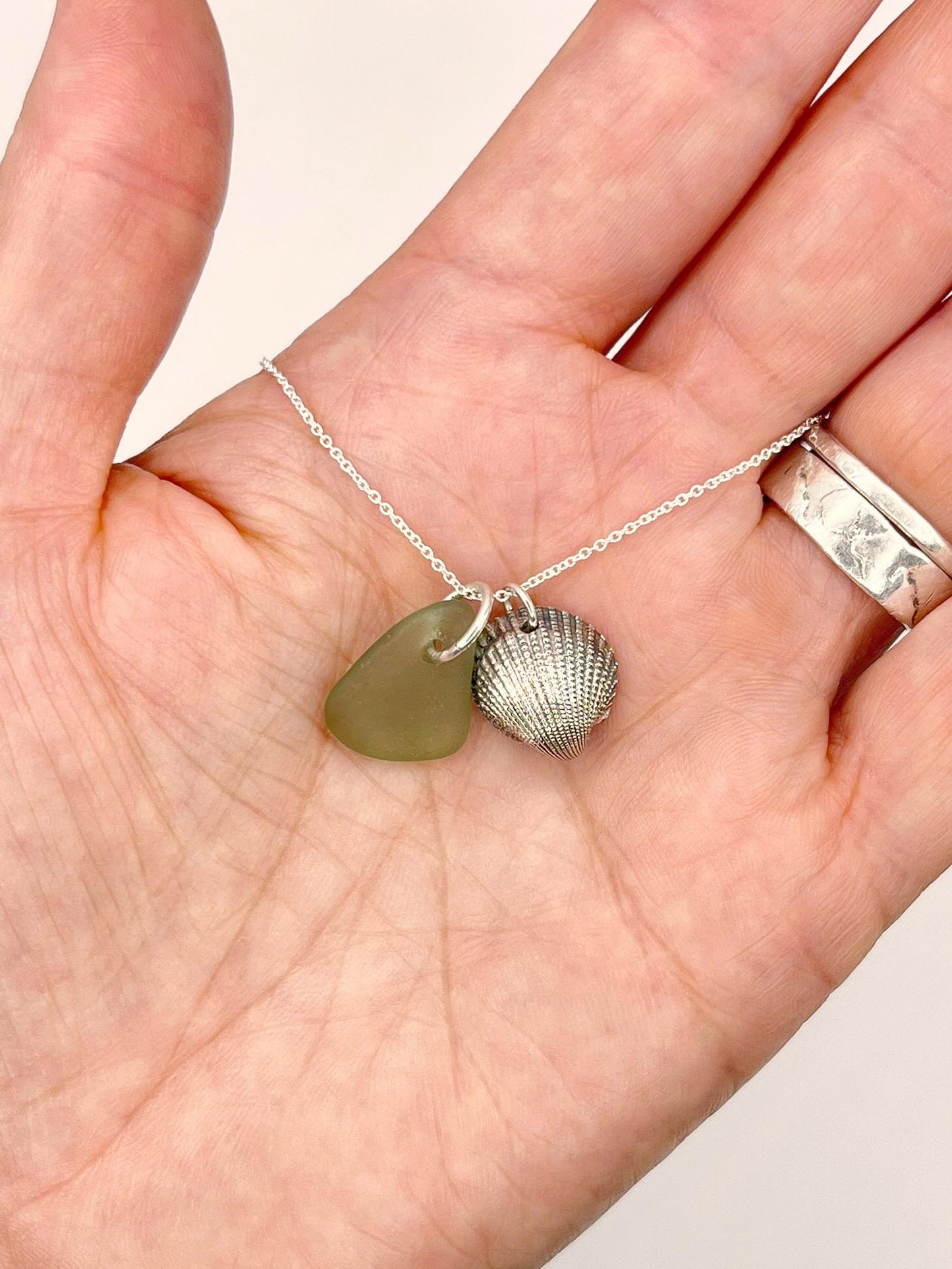 Necklace with green sea glass and a silver shell pendant held in a hand.