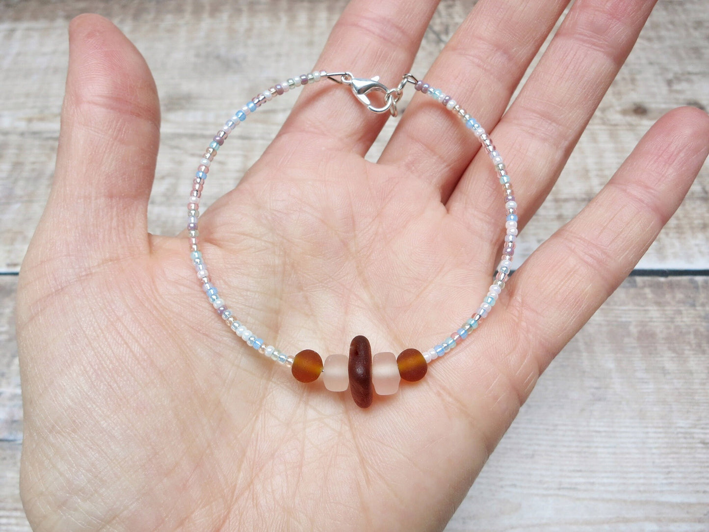 Hand holding bracelet with pastel seed beads and burnt orange sea glass against a textured background