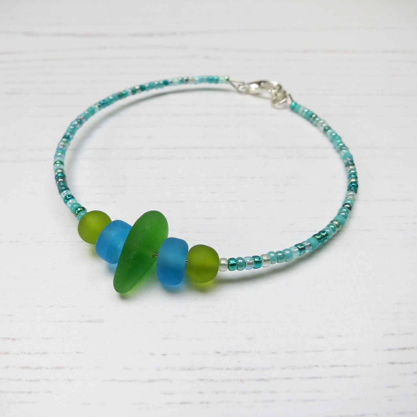 Bracelet with green sea glass and turquoise and green glass beads laid against a white background