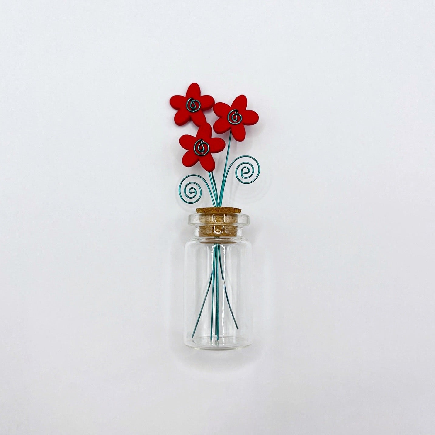 Small glass bottle with red wooden flowers on a white background