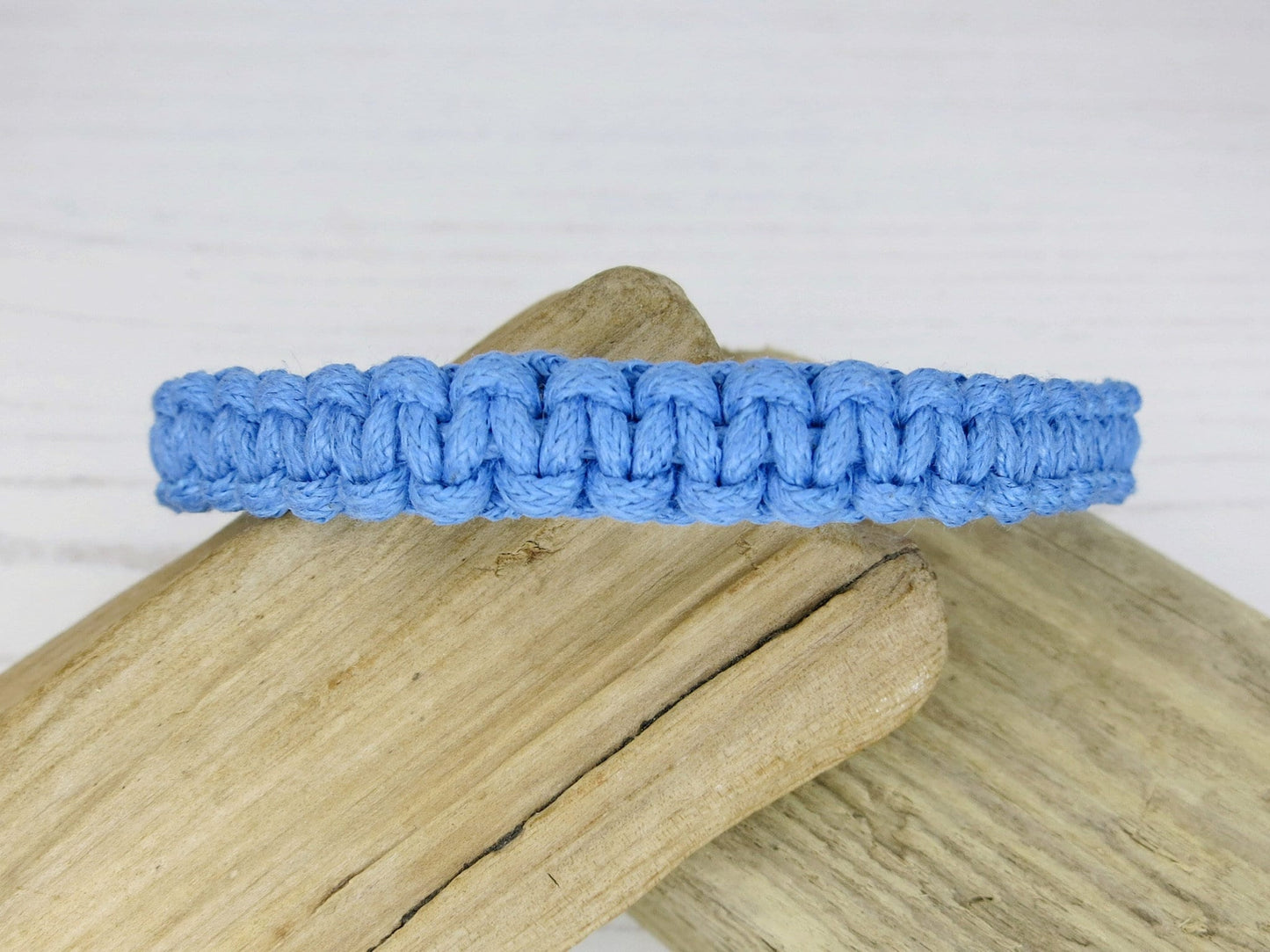 Blue macrame bracelet on a piece of driftwood with a white background