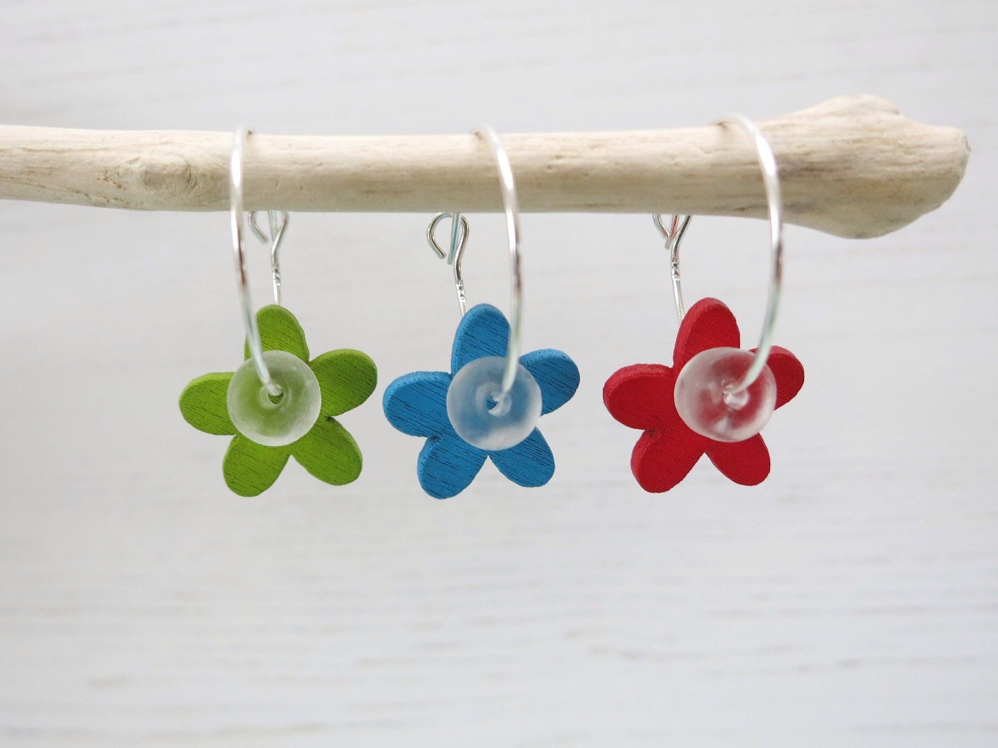 Three colourful button flower earrings hanging on driftwood against a light background