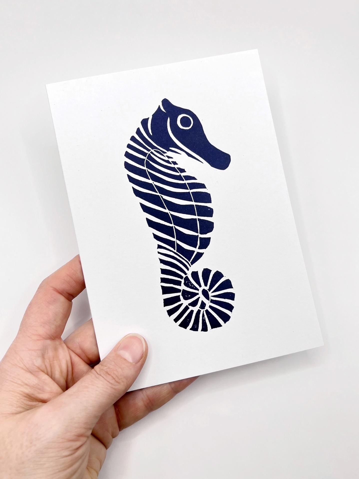 Hand holding a card with a blue seahorse design on a white background