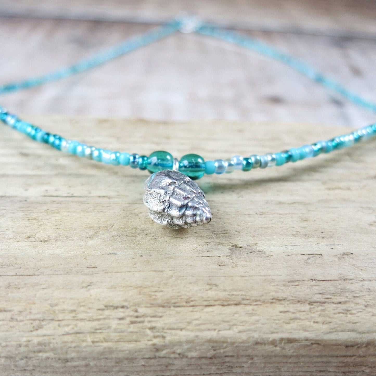 Close up of turquoise beaded necklace with a silver shell charm laid on a wooden surface