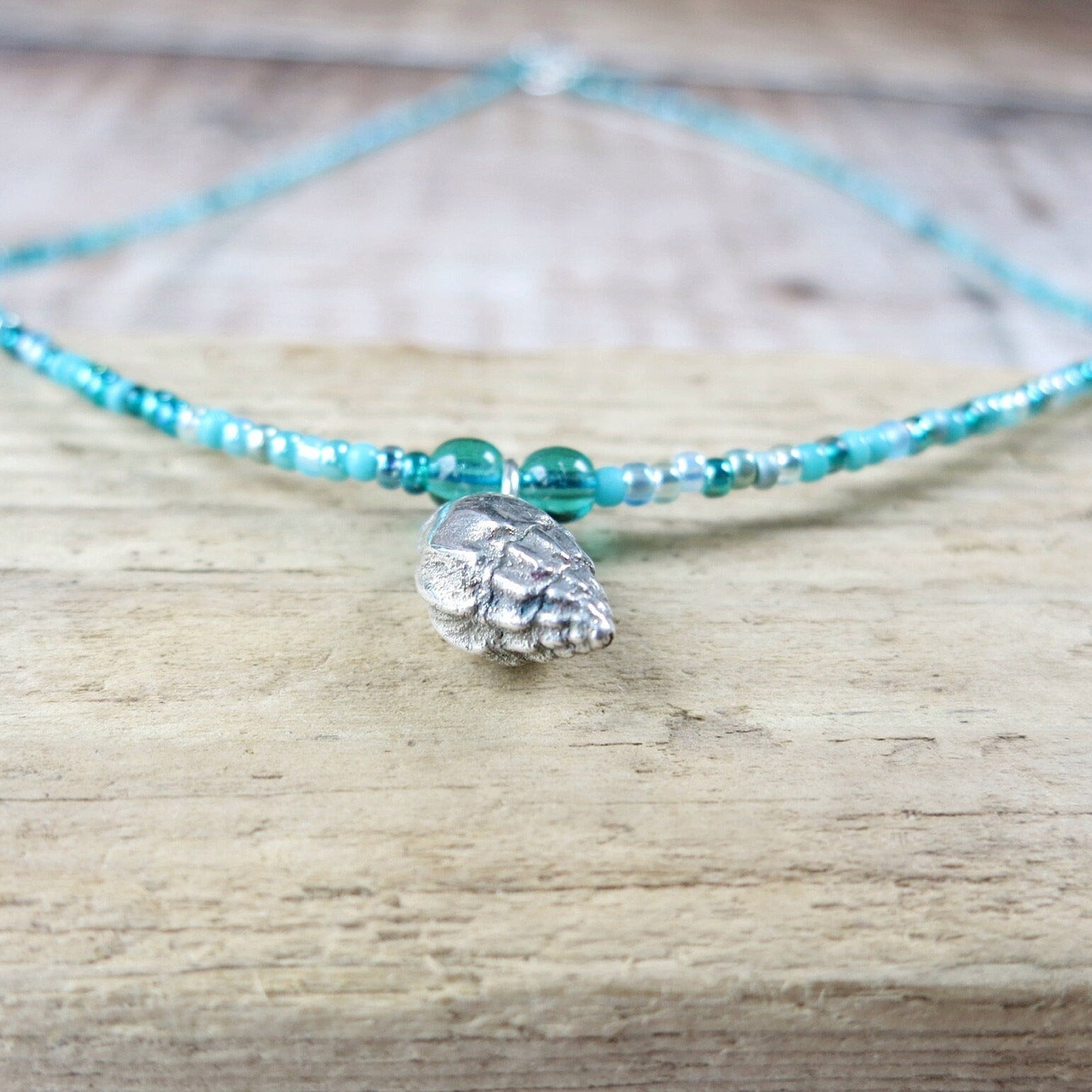 Close up of turquoise beaded necklace with a silver shell charm laid on a wooden surface