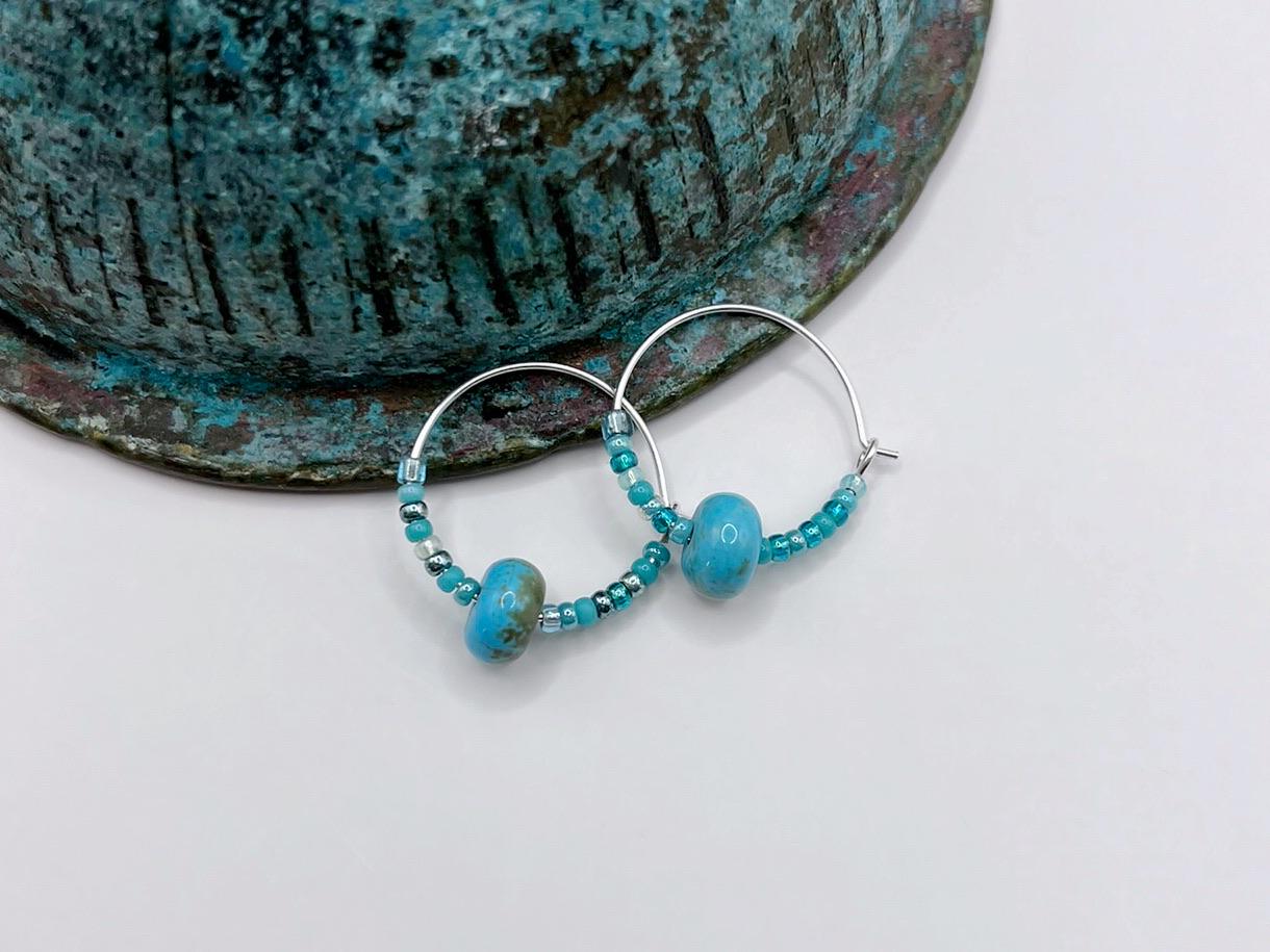 Turquoise beaded hoop earrings laid against a copper bowl on a white surface 