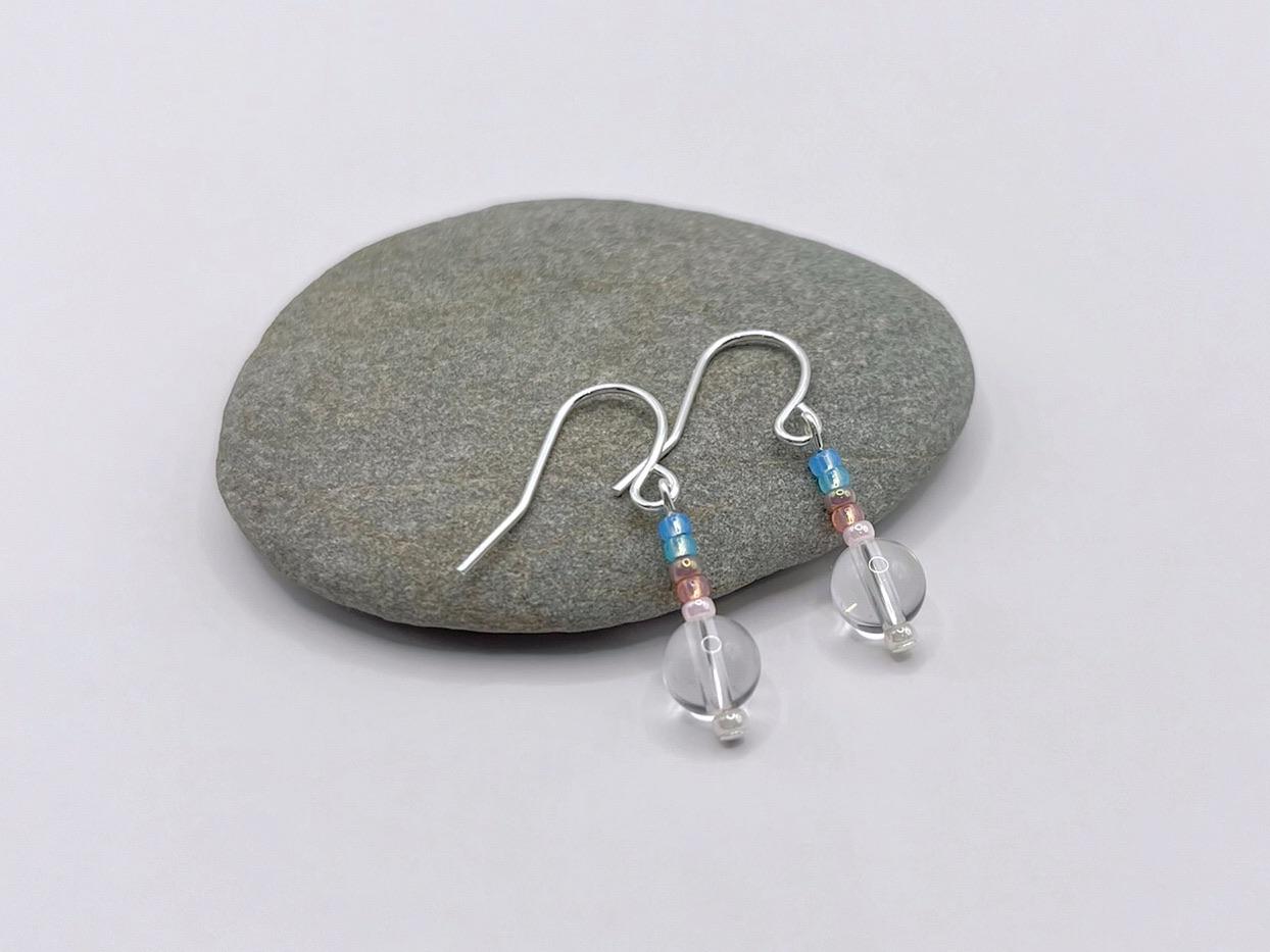 Silver earrings with crystal and pastel seed beads laid on a grey pebble
