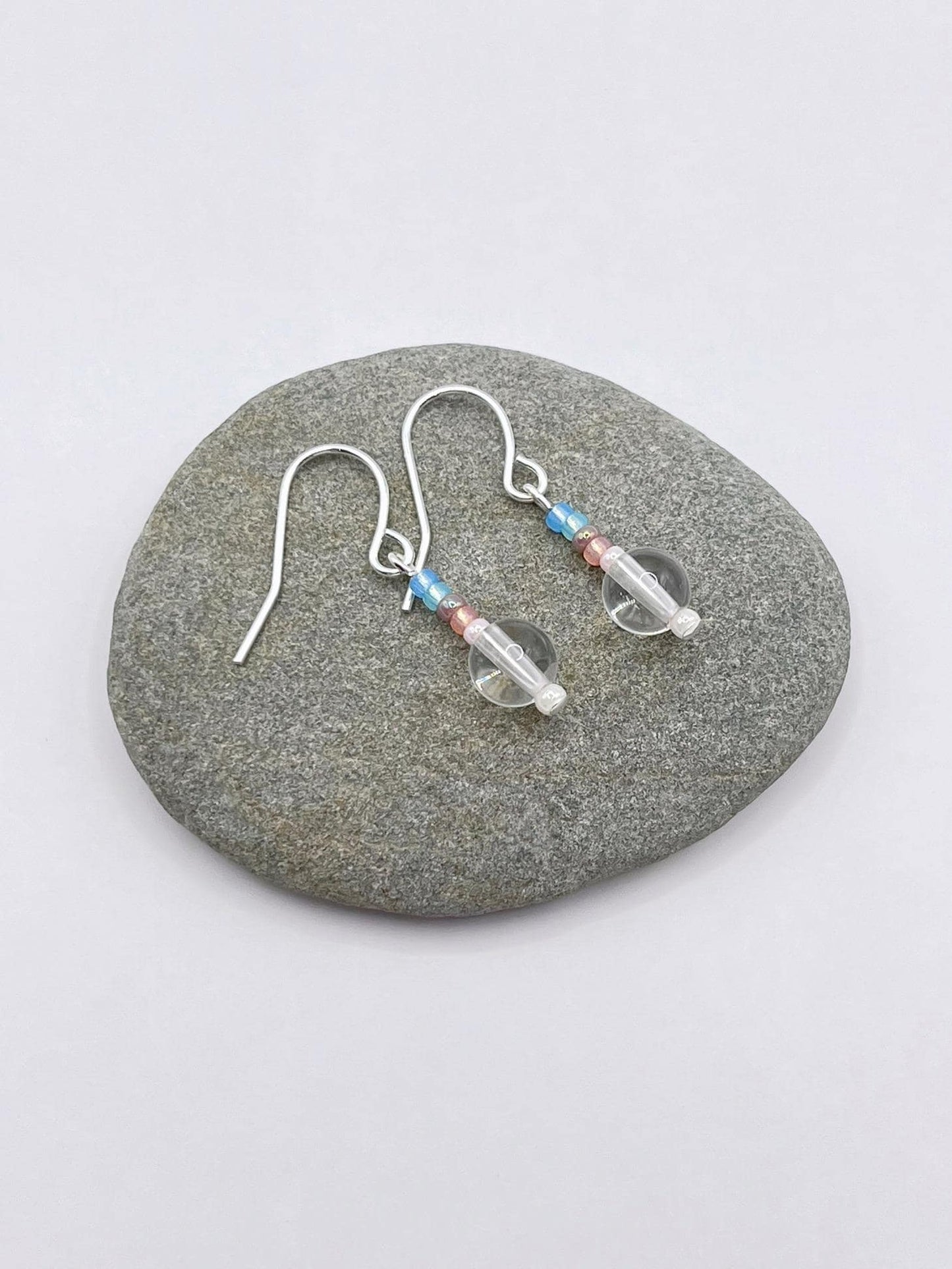 Pair of crystal and pastel seed bead earrings laid on a grey pebble