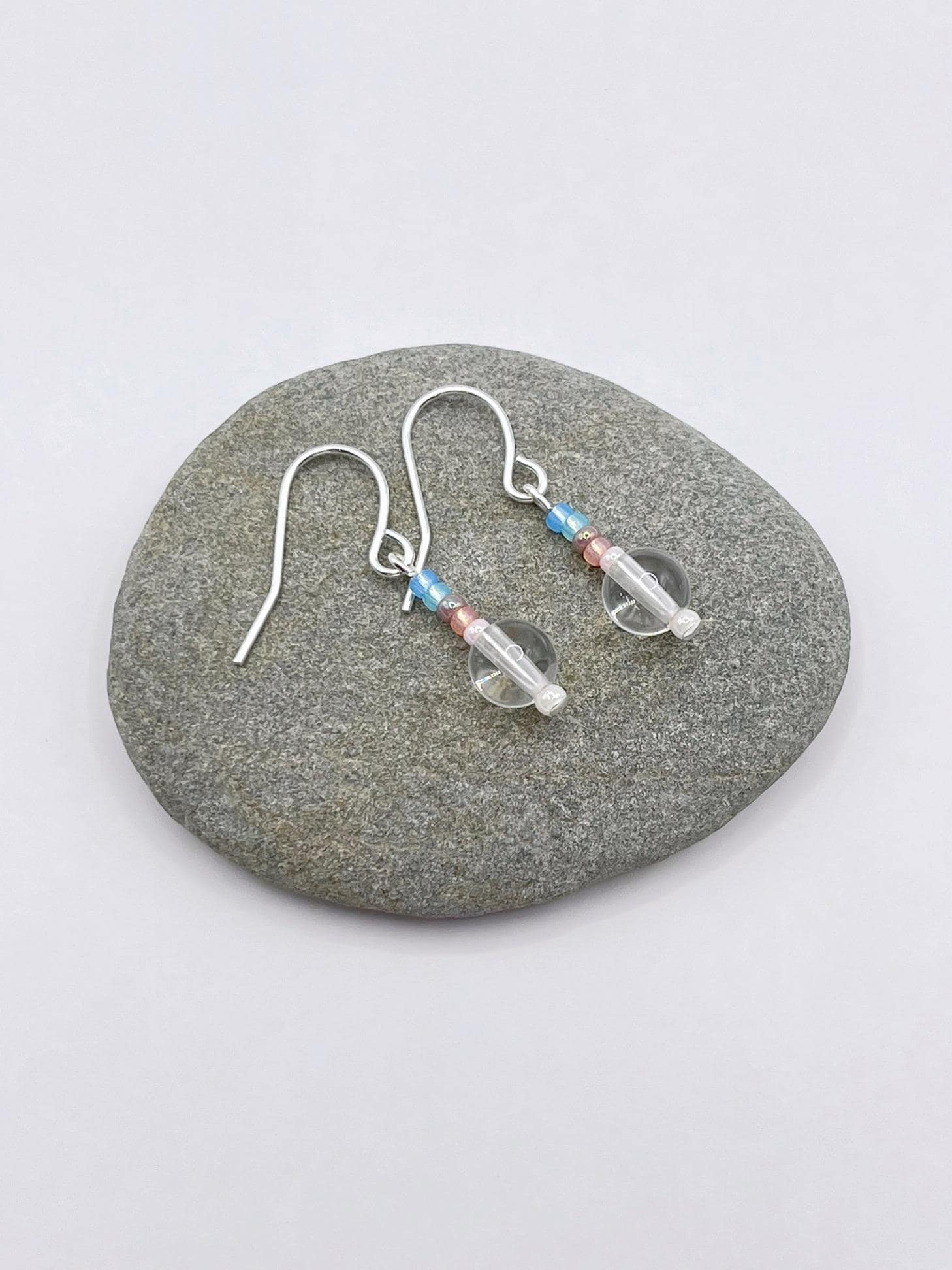 Pair of crystal and pastel seed bead earrings laid on a grey pebble