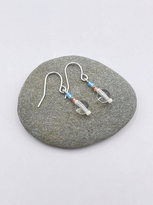 Pair of crystal and pastel seed bead earrings laid on a grey pebble