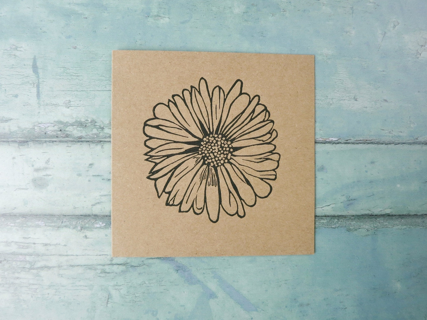 Kraft paper card with an original daisy lino print laid on a textured surface. 