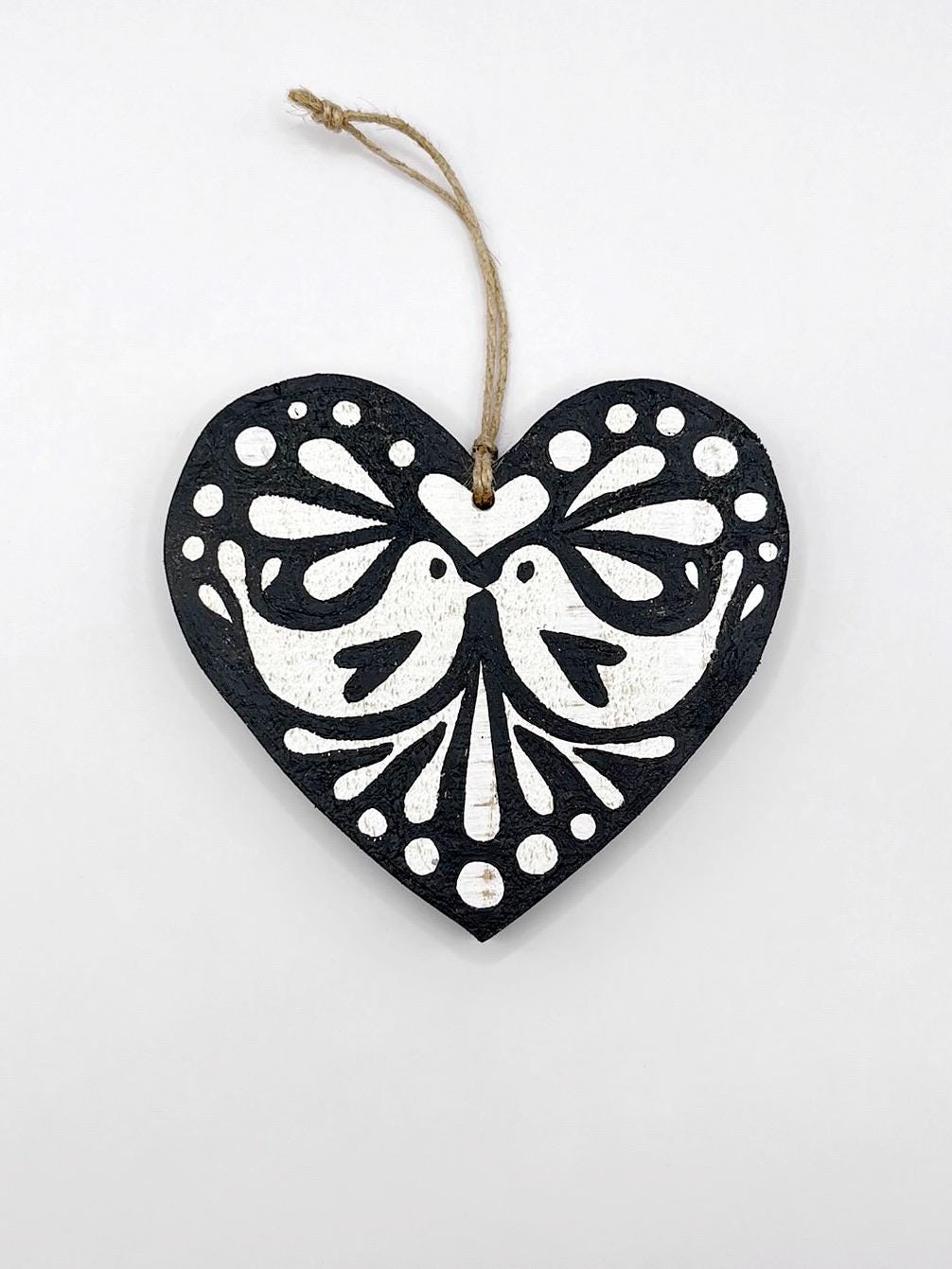 Black heart-shaped wooden hanging decoration with folk style love bird print   laid on a white background