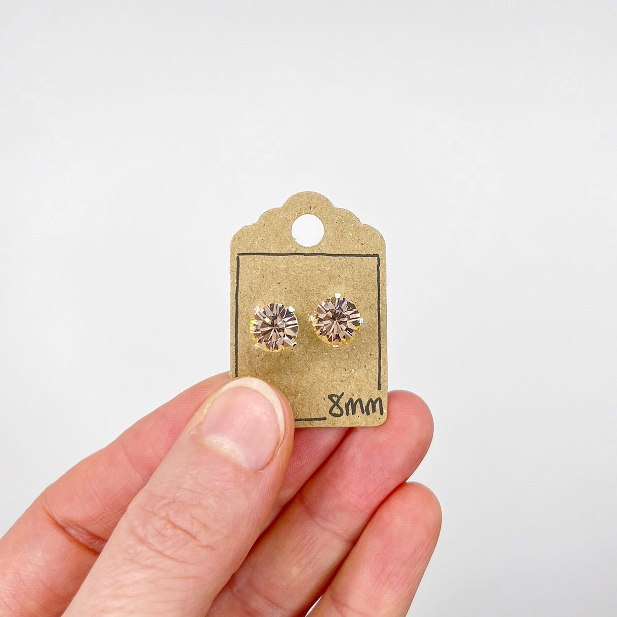 Cut glass stud earrings on a card held by a hand against a white background