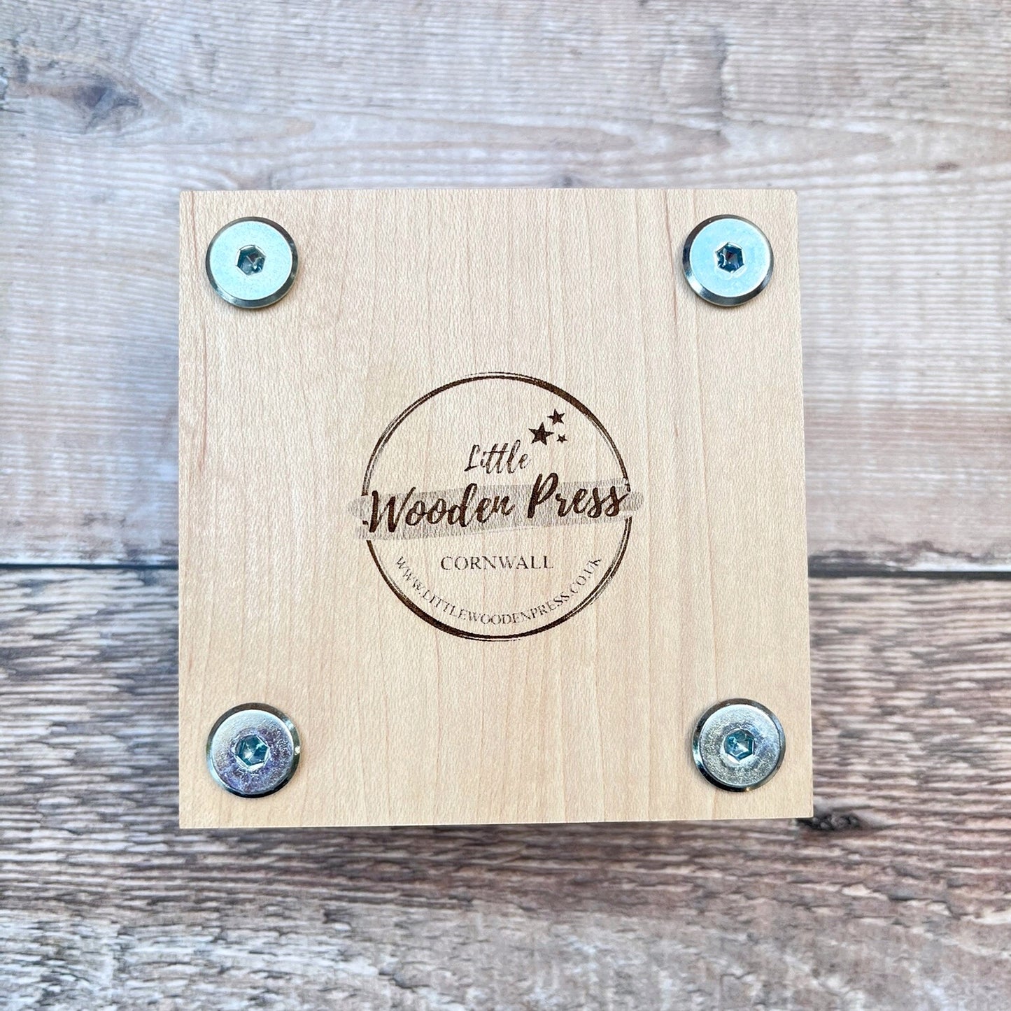 Underneath of the wooden flower press showing the  'Little Wooden Press' branding, laid on a textured surface
