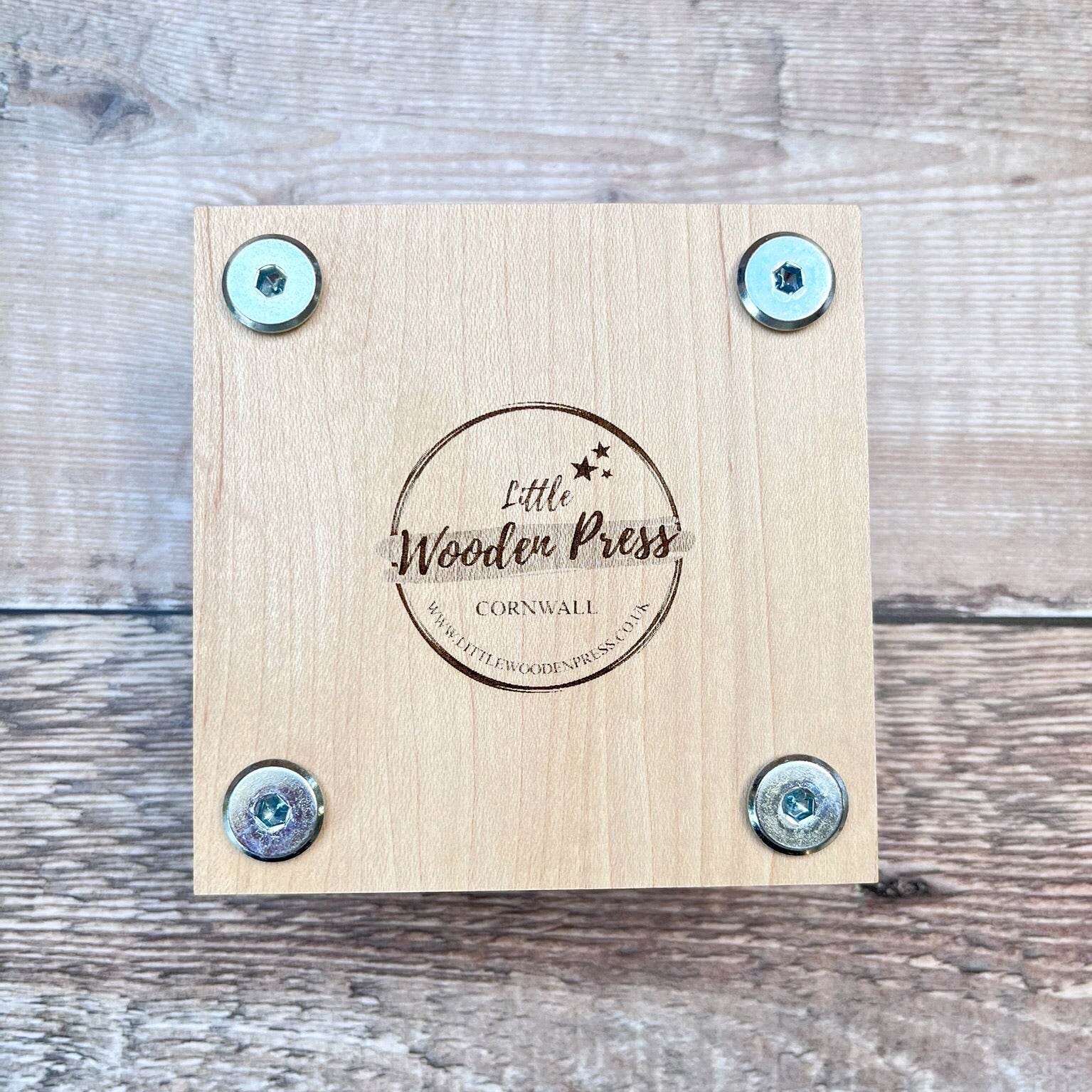 Underneath of the wooden flower press showing the  'Little Wooden Press' branding, laid on a textured surface
