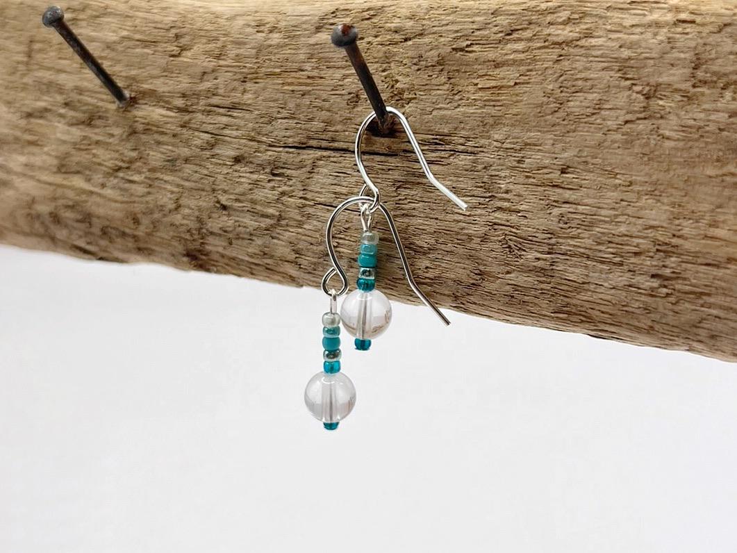 Silver earrings with beads hanging on a piece of driftwood.