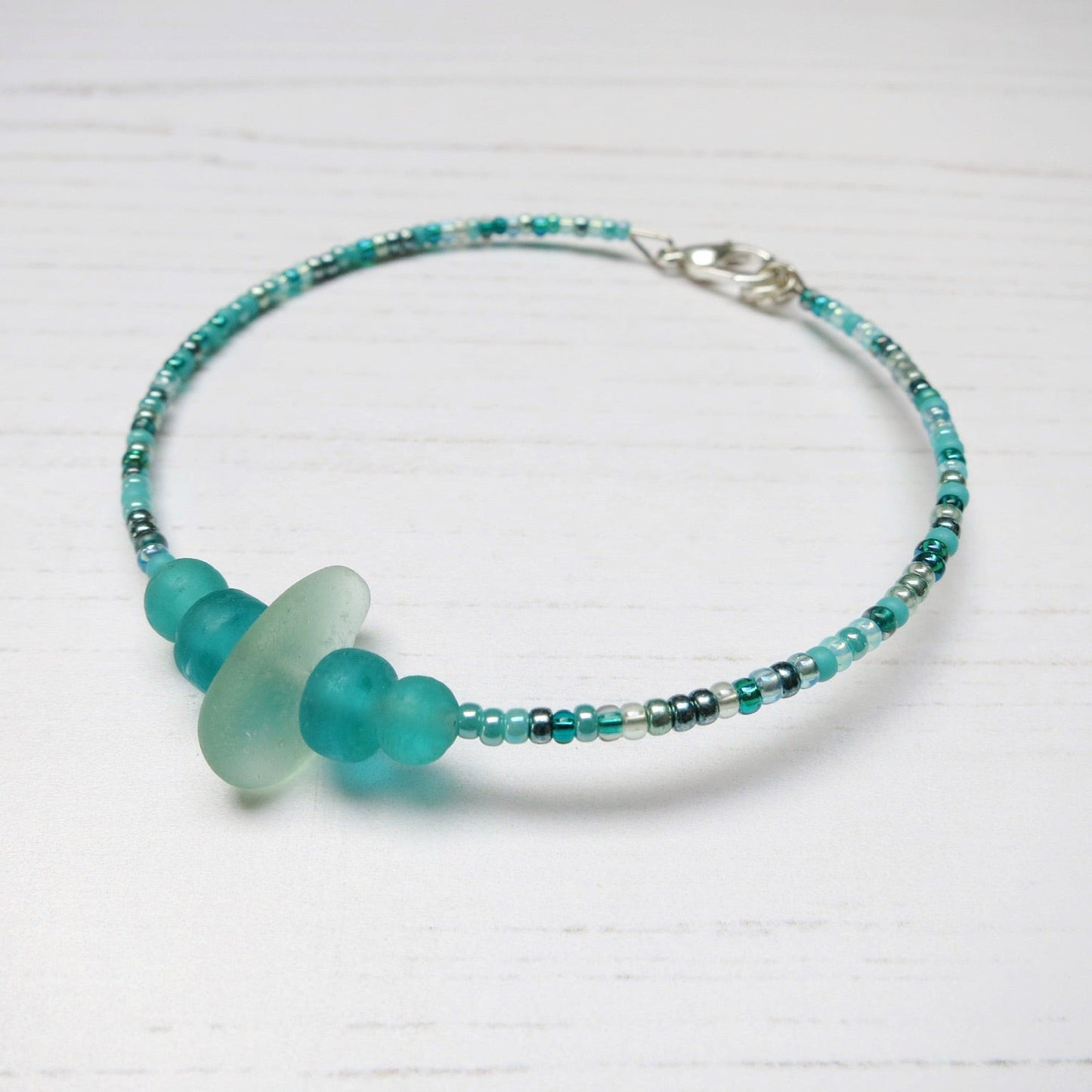 Bracelet with pale sea foam sea glass and sea green and turquoise glass beads laid on a white background
