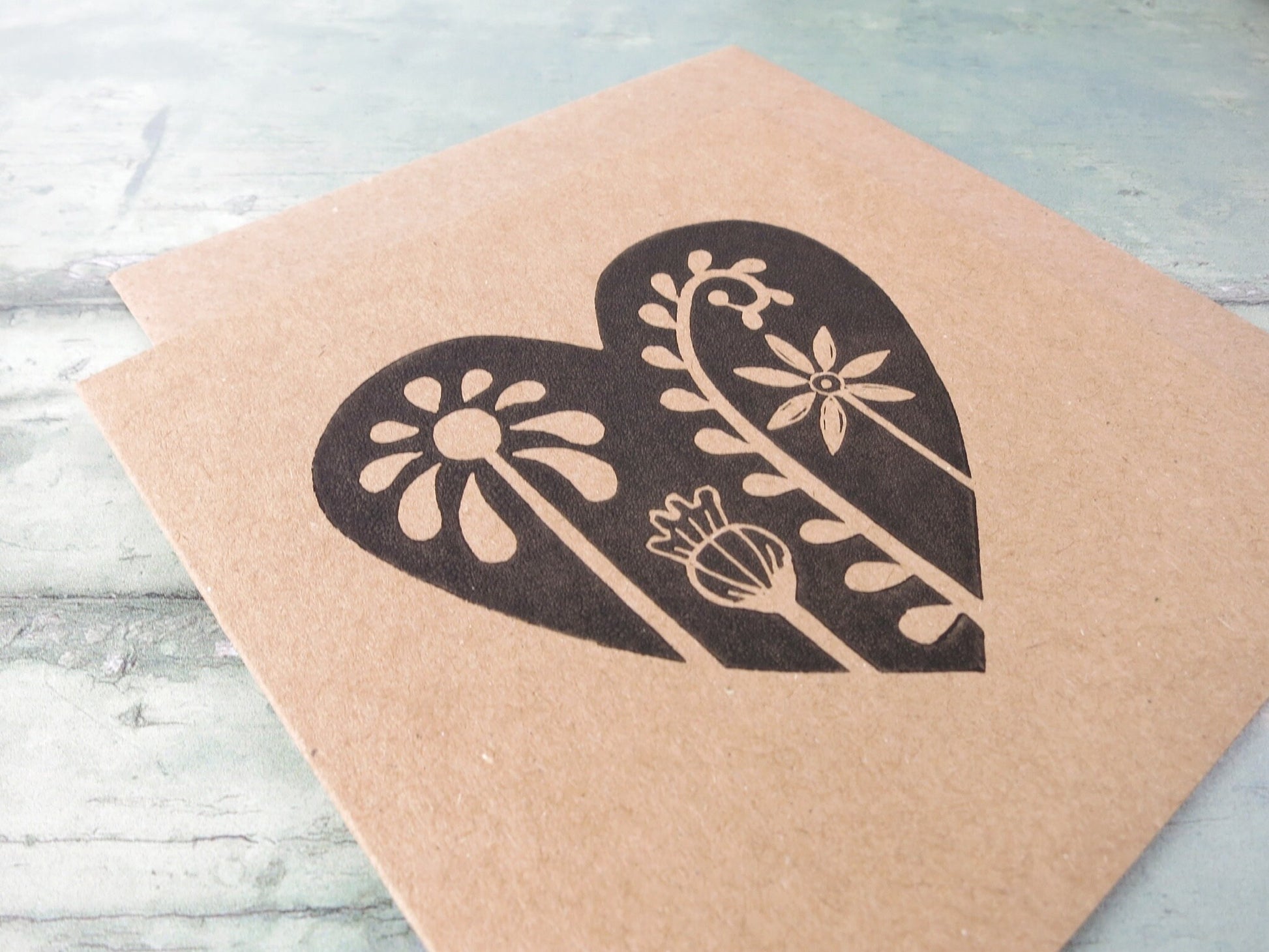 Close up of Kraft paper card with an original lino printed floral heart design laid on  a textured surface.