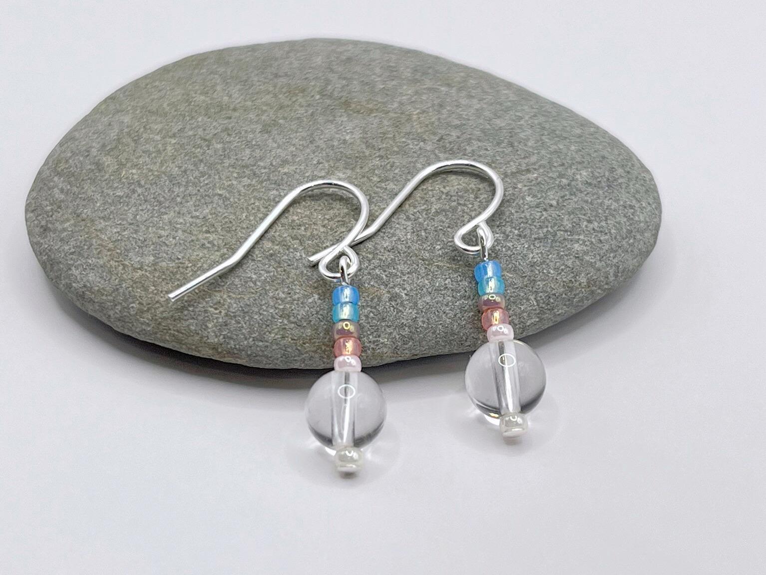 Pair of earrings with crystal and pastel seed beads laid on a grey pebble