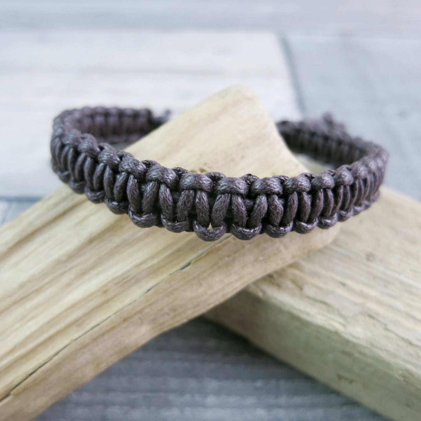Brown macrame bracelet laid on driftwood with a neutral background