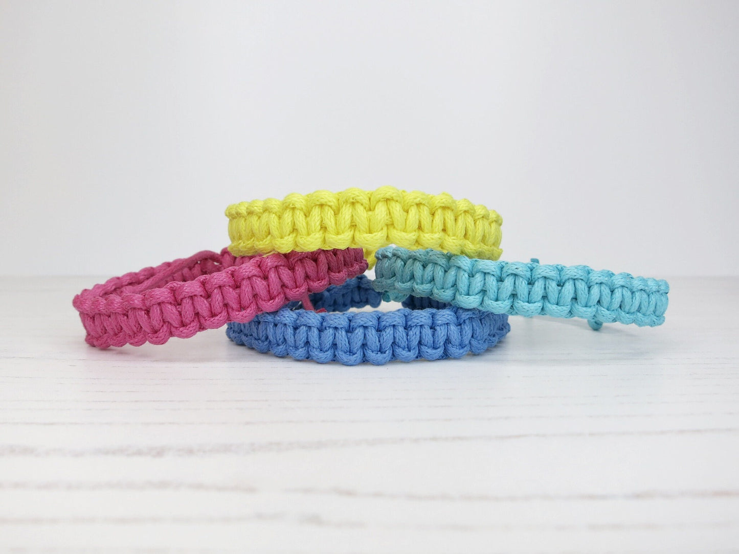 Four colorful macrame bracelets on a light wooden surface