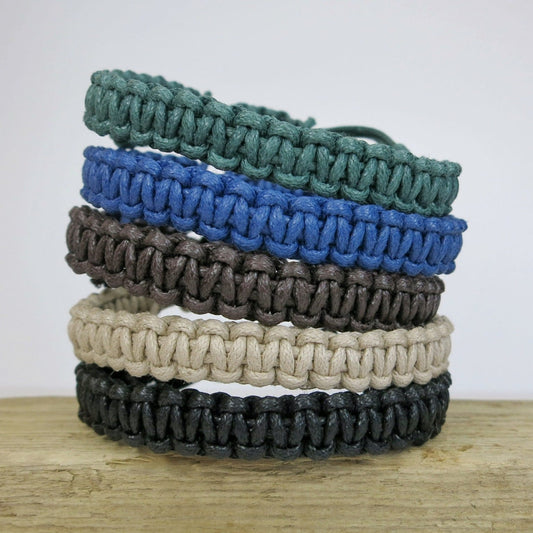 Stack of four macrame bracelets in green, blue, brown, natural and black on a wooden surface.