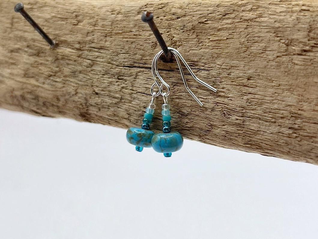 Turquoise beaded earrings hanging on driftwood