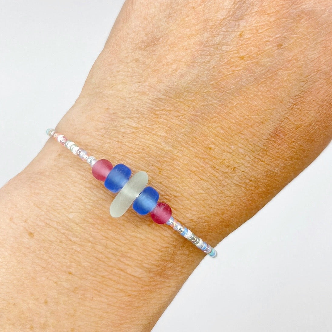 Close up of a pastel beaded bracelet with pink and blue frosted glass beads and a piece of sea foam coloured Cornish sea glass, worn on my wrist.