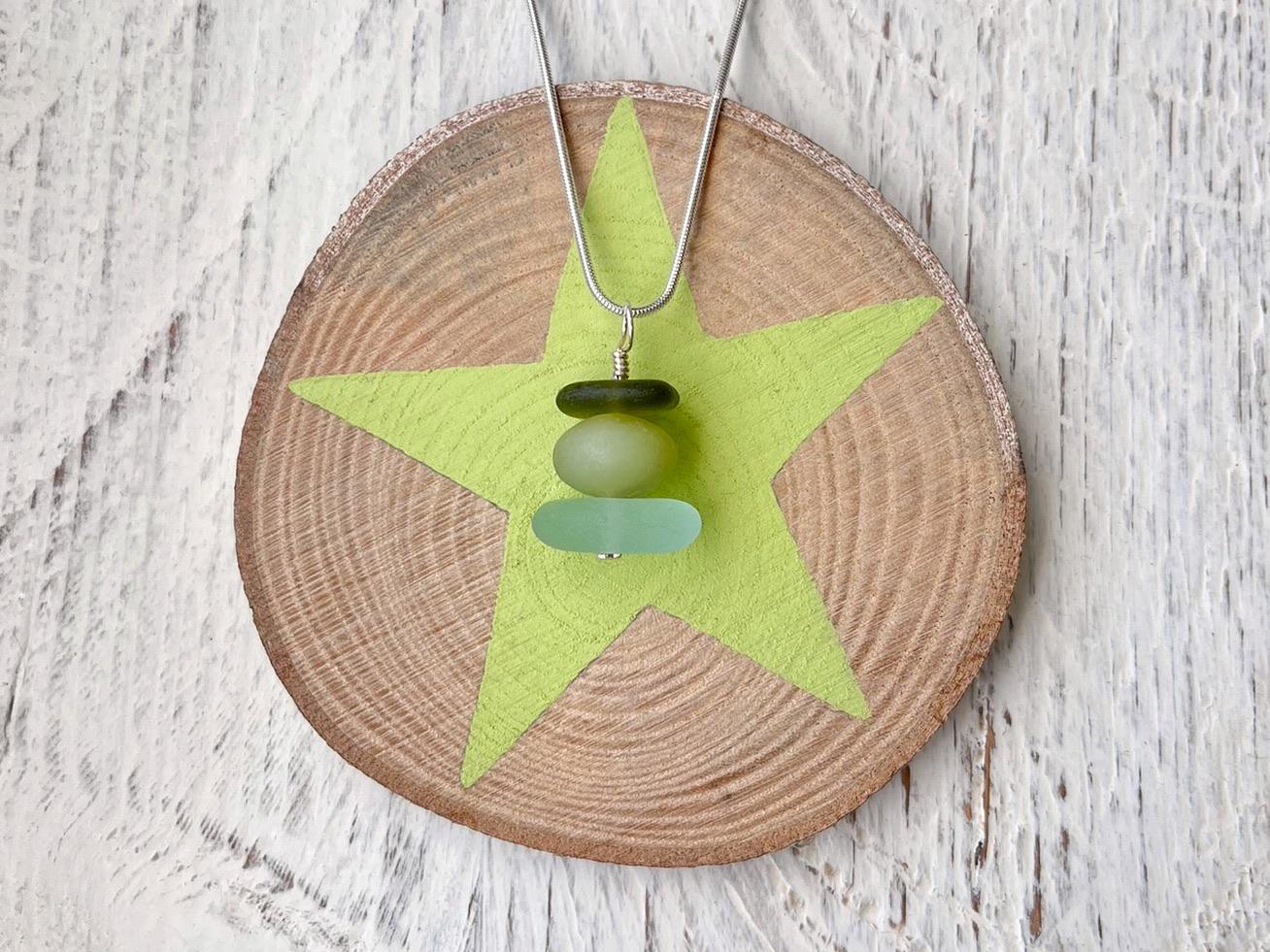 Necklace with green sea glass and a Jade bead laid on a star printed slice of wood against a textured surface.