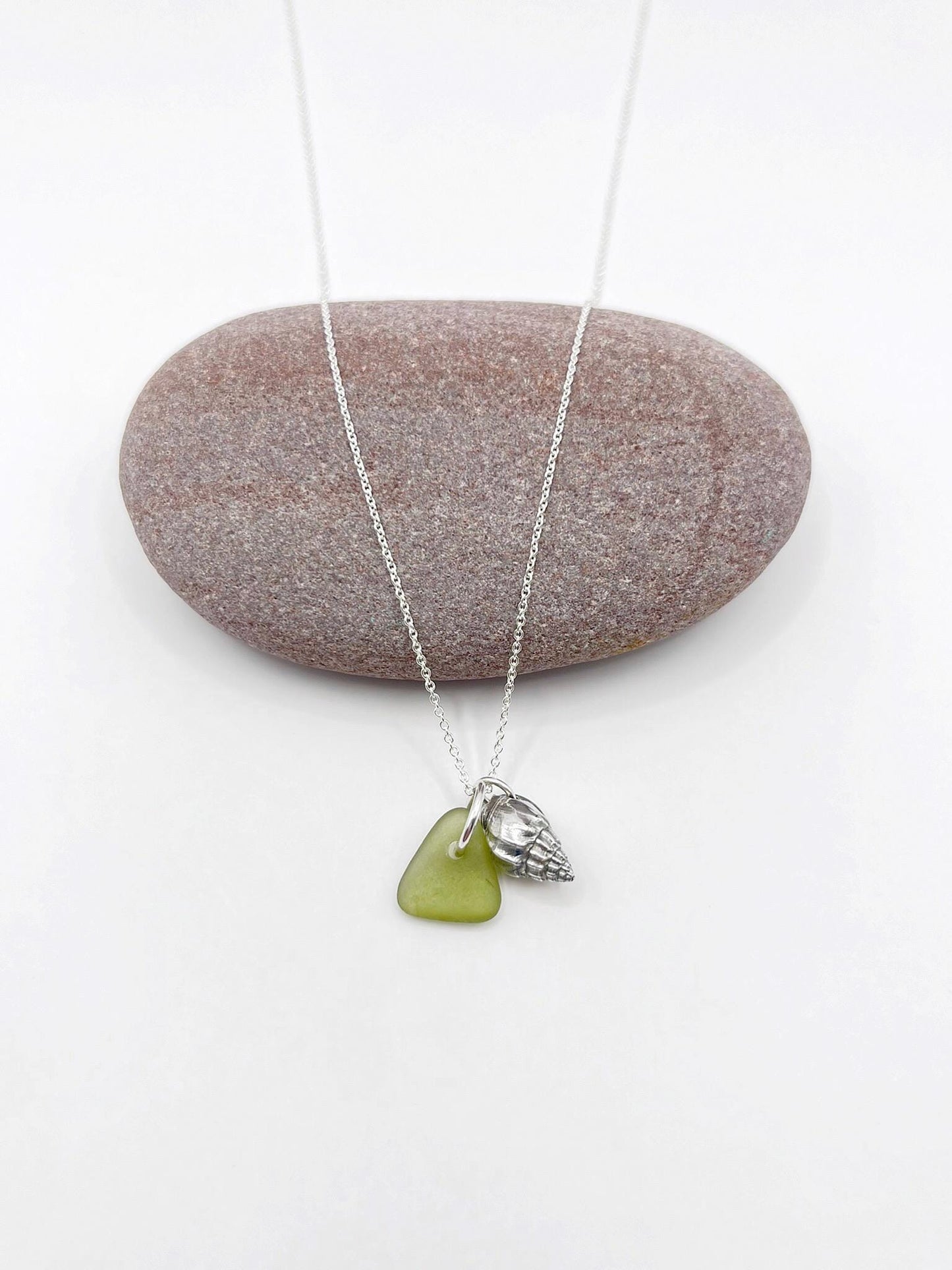Necklace with olive green sea glass and a silver shell pendant laid on a white background