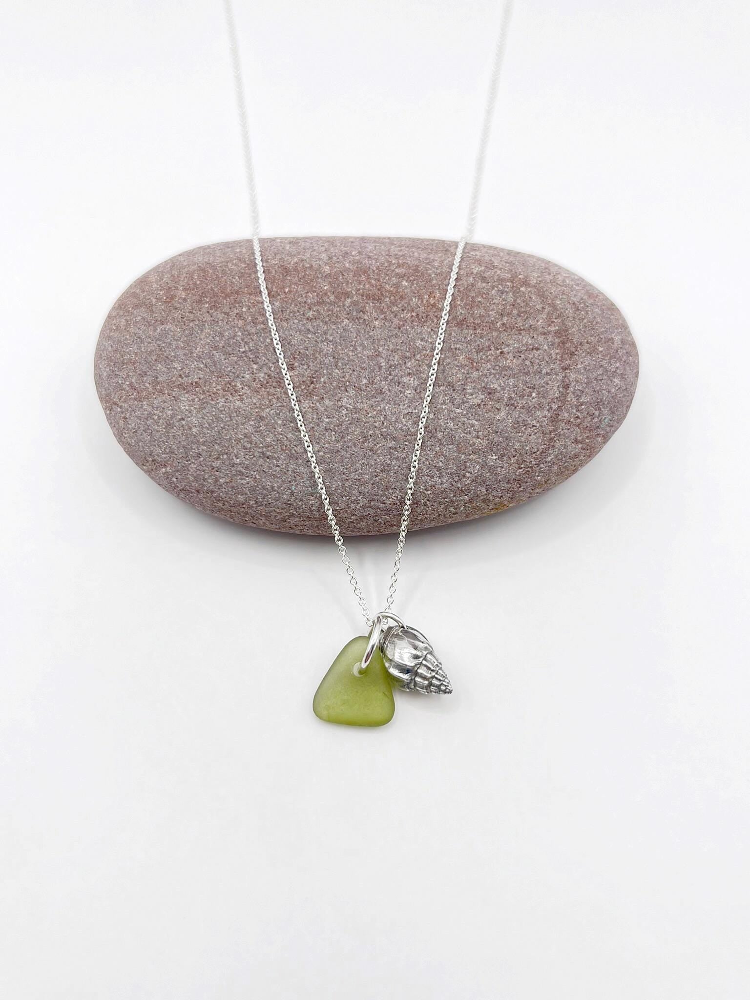 Necklace with olive green sea glass and a silver shell pendant laid on a white background
