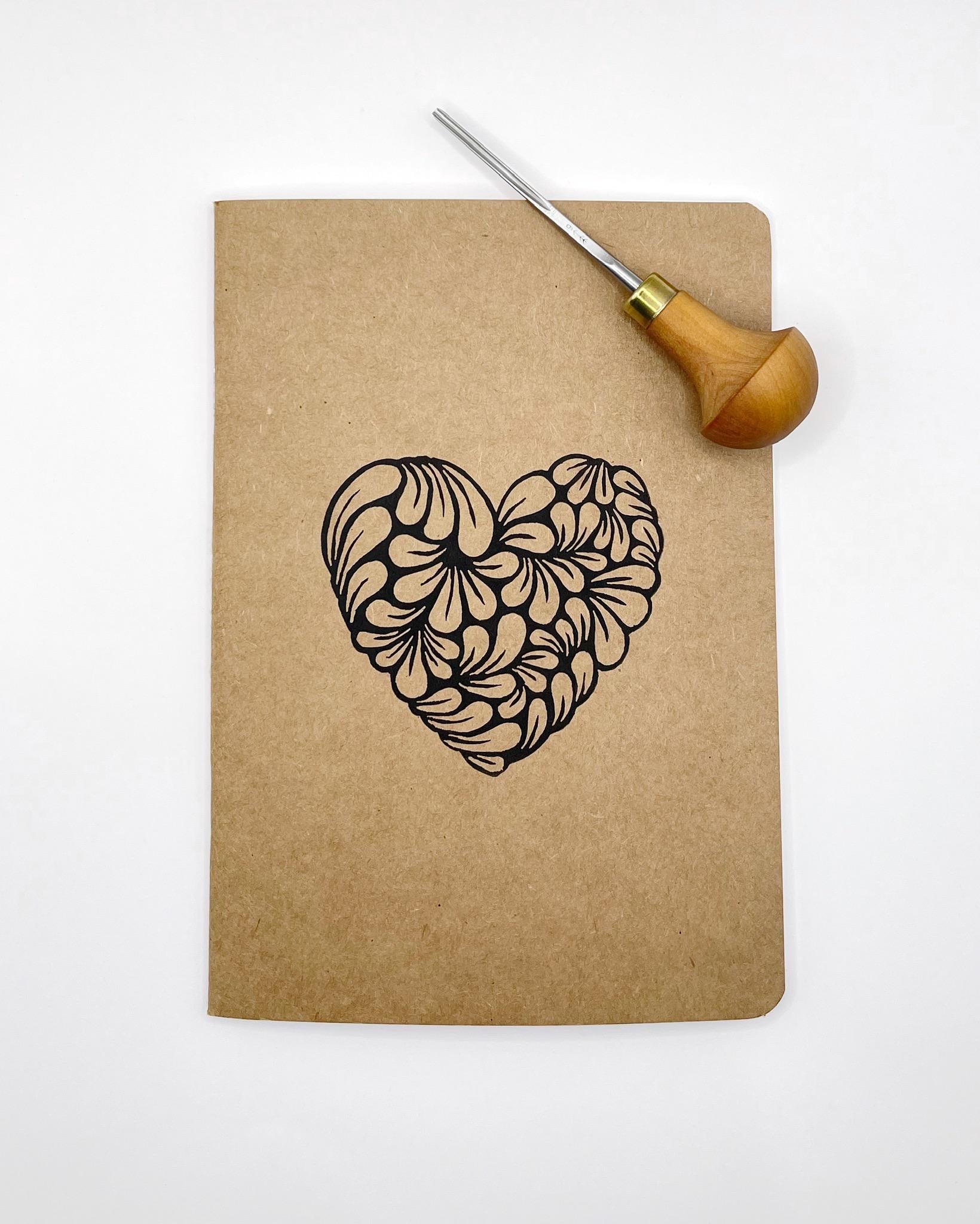 Kraft paper notebook with an original lino printed heart design. Photo includes the lino cutting tool used and is laid on a white background