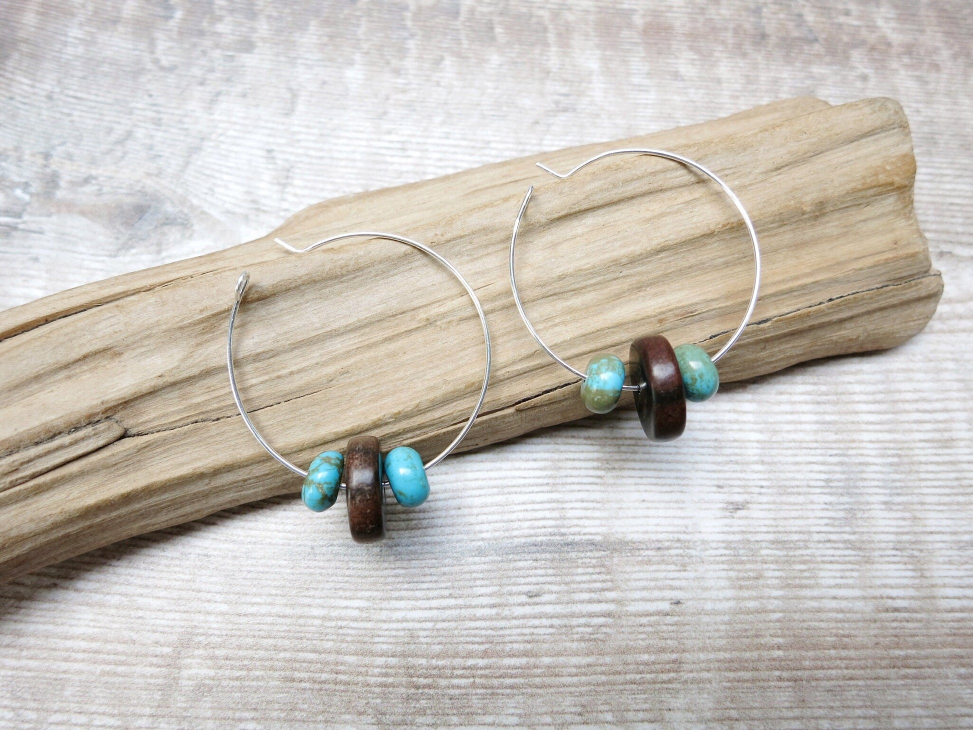 Pair of silver hoop earrings with wooden and turquoise beads laid on a textured surface