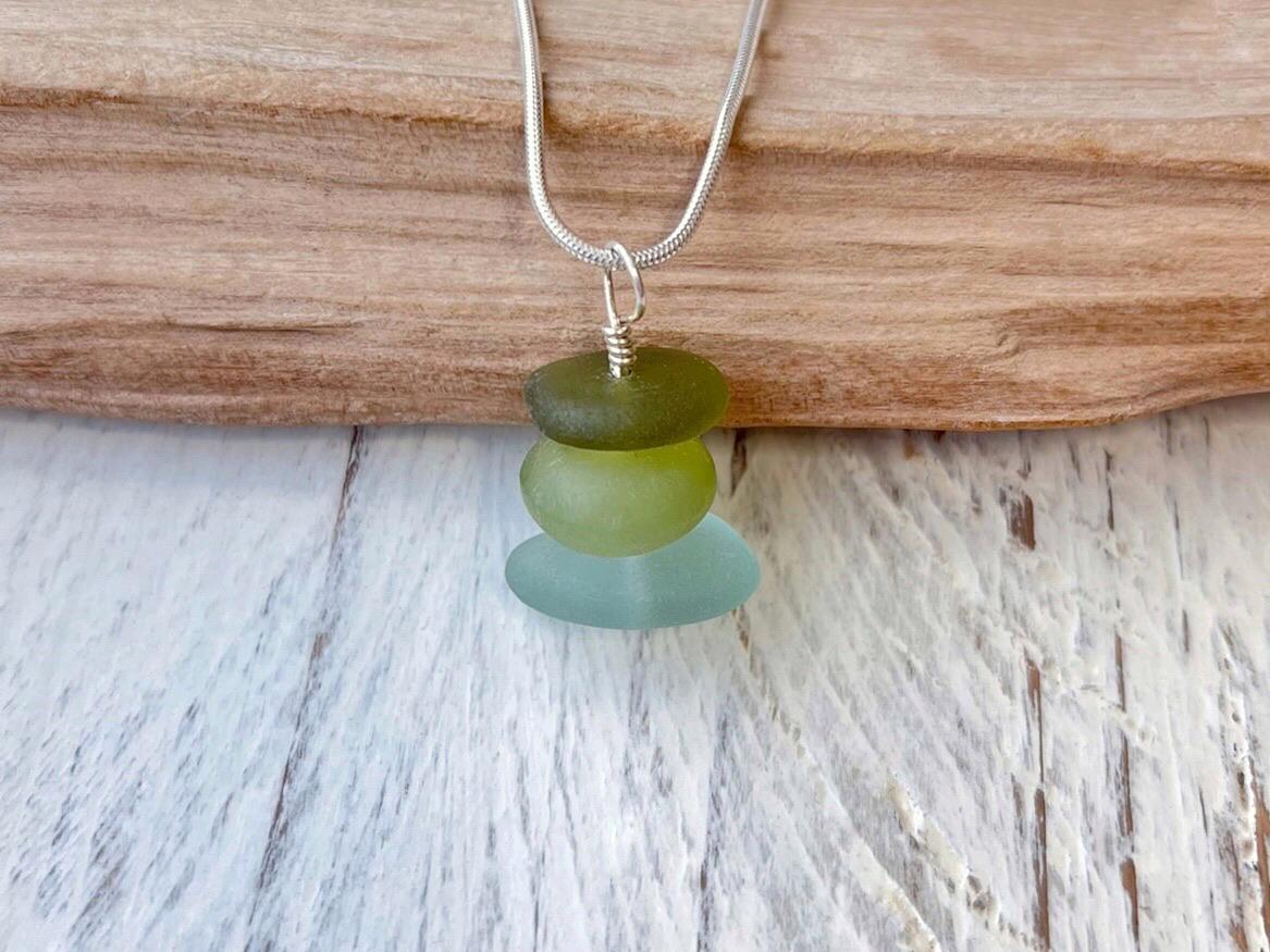 Necklace with green sea glass and a Jade bead laid on driftwood against a textured surface.