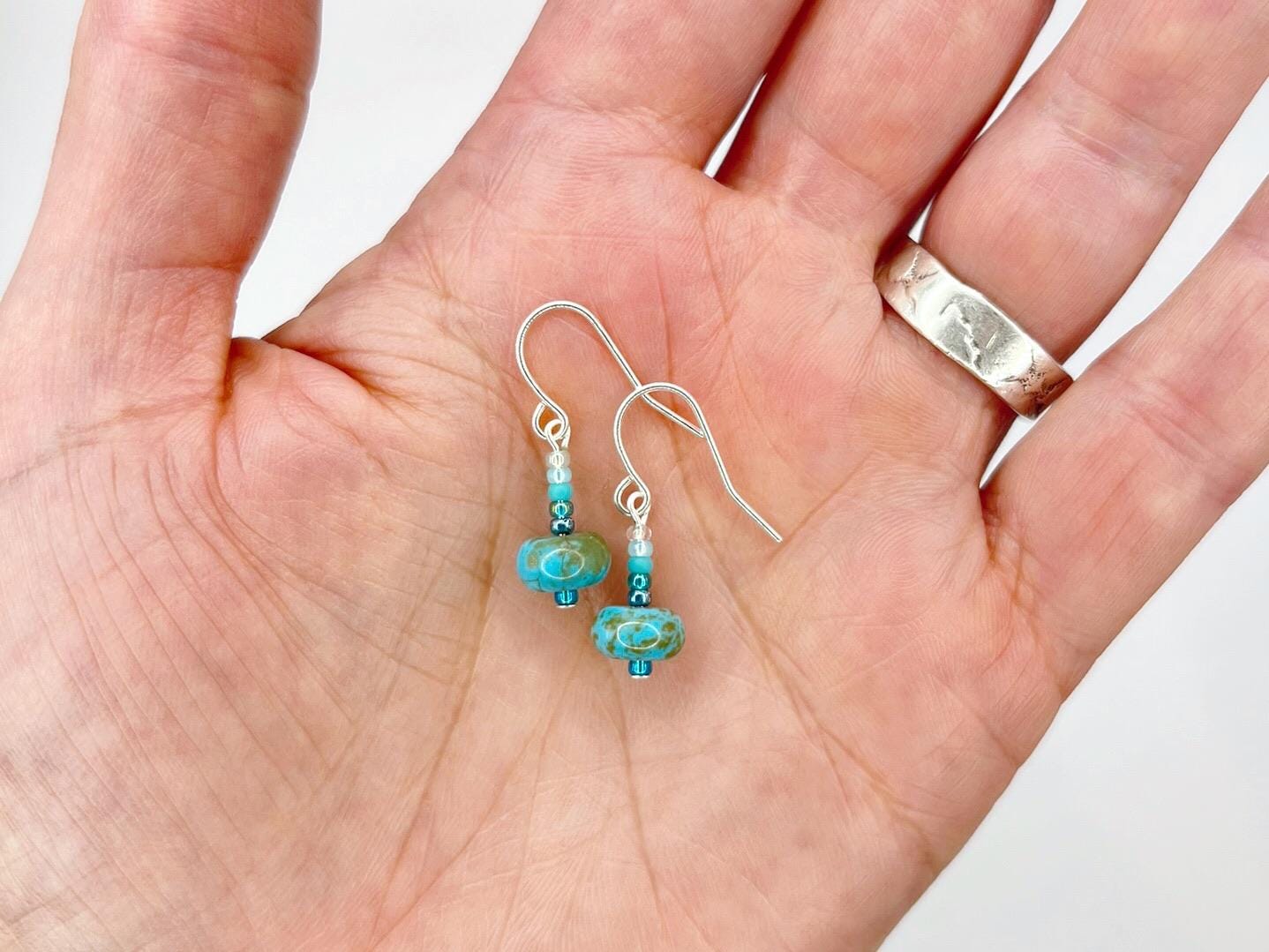 Turquoise beaded earrings held in a hand against a white background