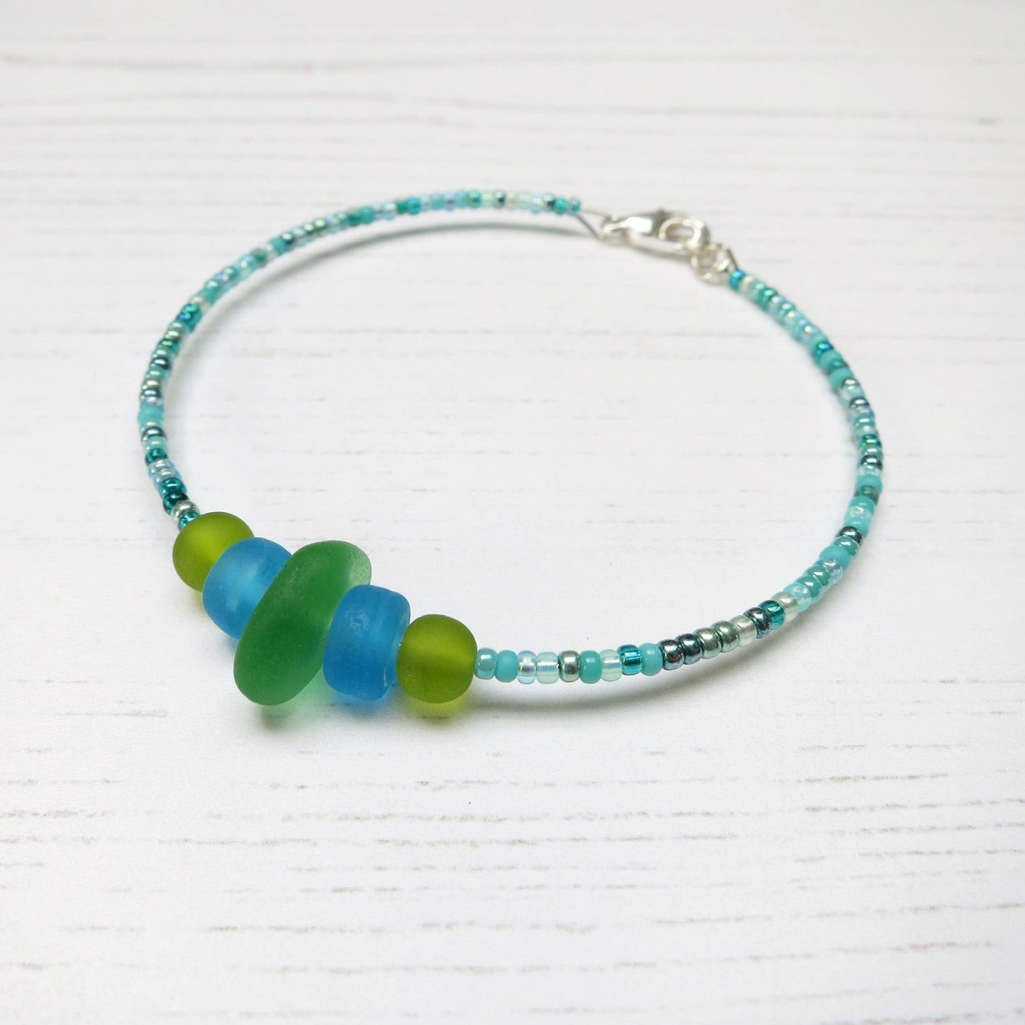 Bracelet with green sea glass and turquoise and green glass beads laid on a white background