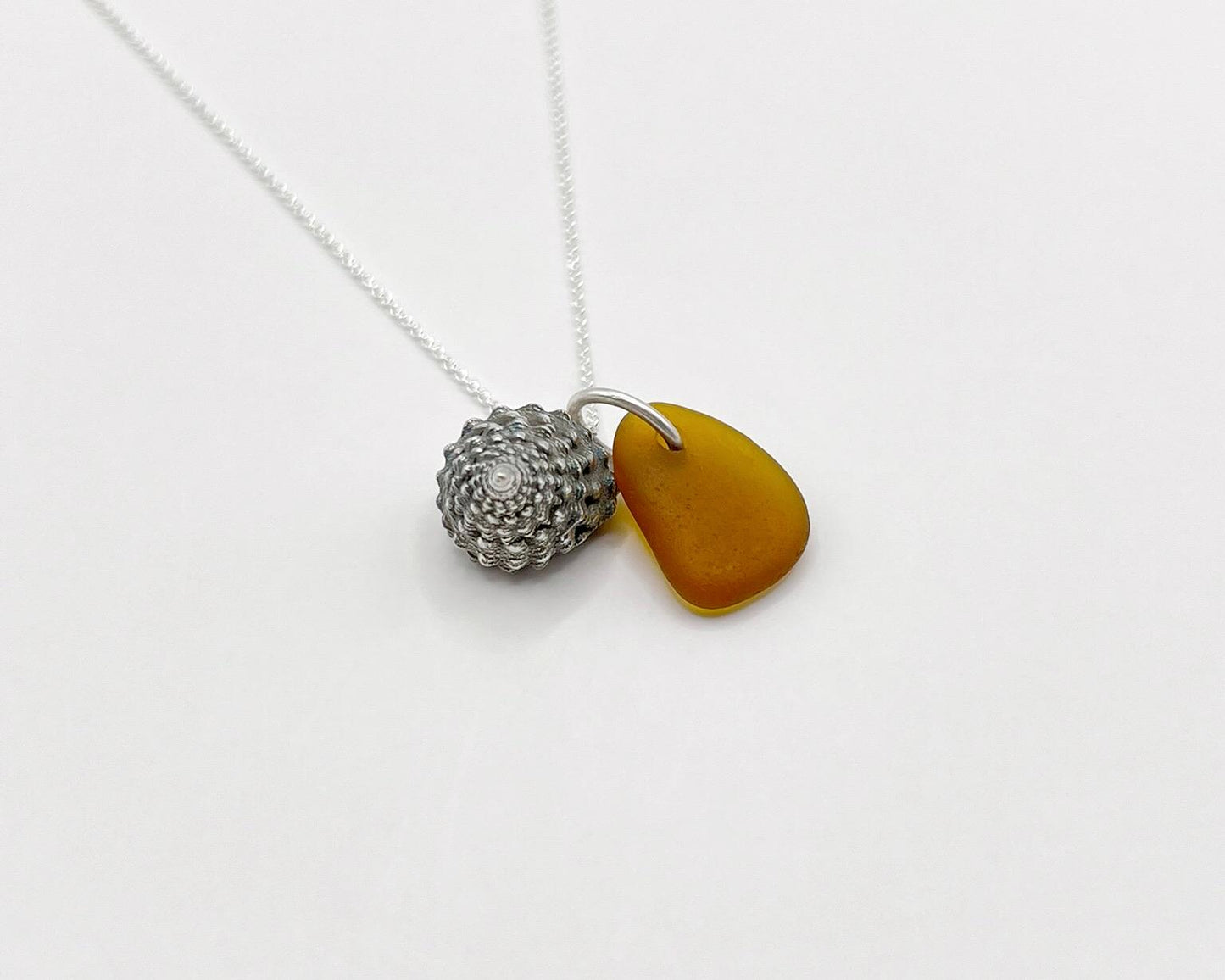 Necklace with burnt orange sea glass and silver shell pendant laid on a white background