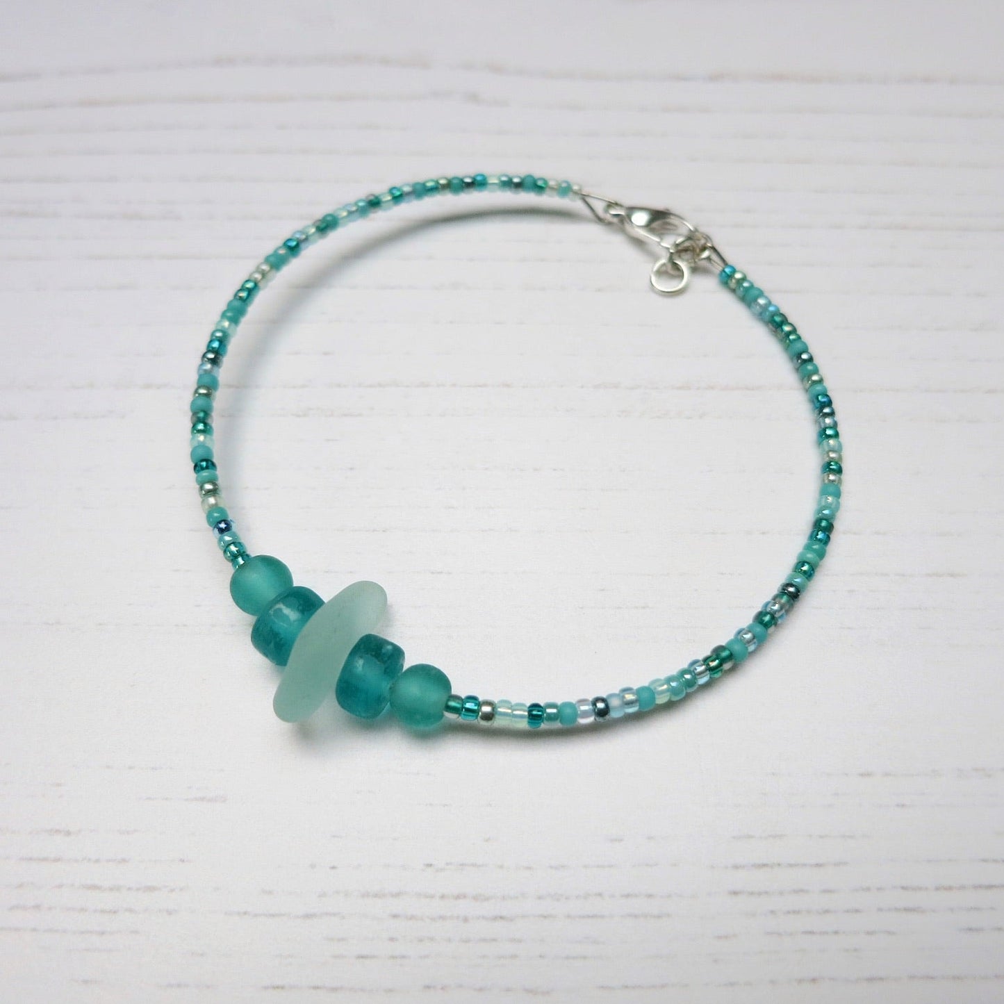 Bracelet with pale sea foam sea glass and sea green and turquoise glass beads laid on a white background
