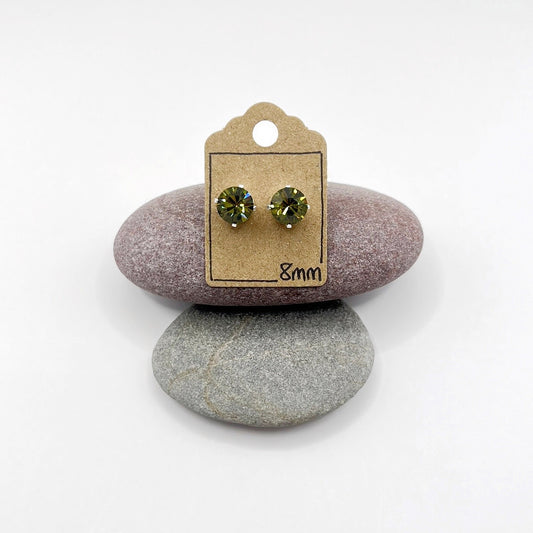Pair of olive green cut glass earrings on a cardboard backing card, placed on two stones.