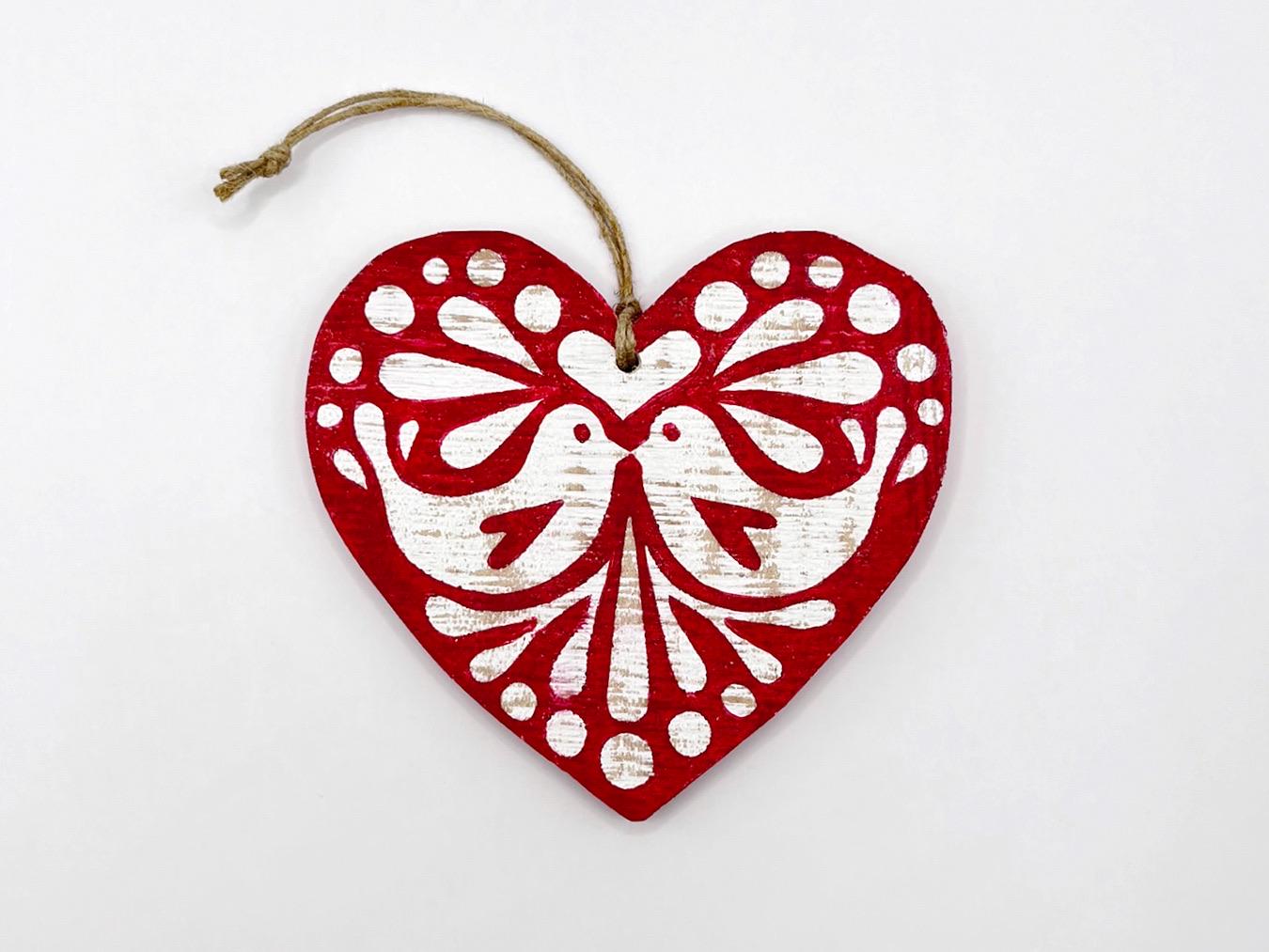 Red heart-shaped wooden hanging decoration with folk style love bird print laid on a white background
