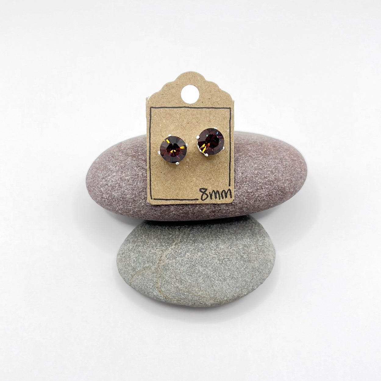 Pair of cut glass stud earrings on a card with stones in the background