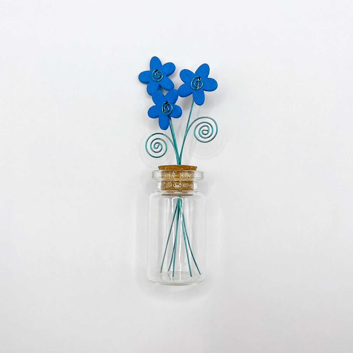 Little glass bottle with three blue wooden flowers against a white background